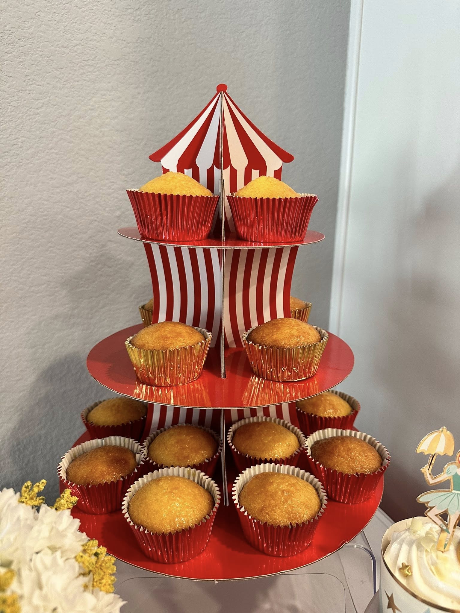 Three-tiered red and white carnival-themed cupcake stand holding cupcakes in metallic red liners