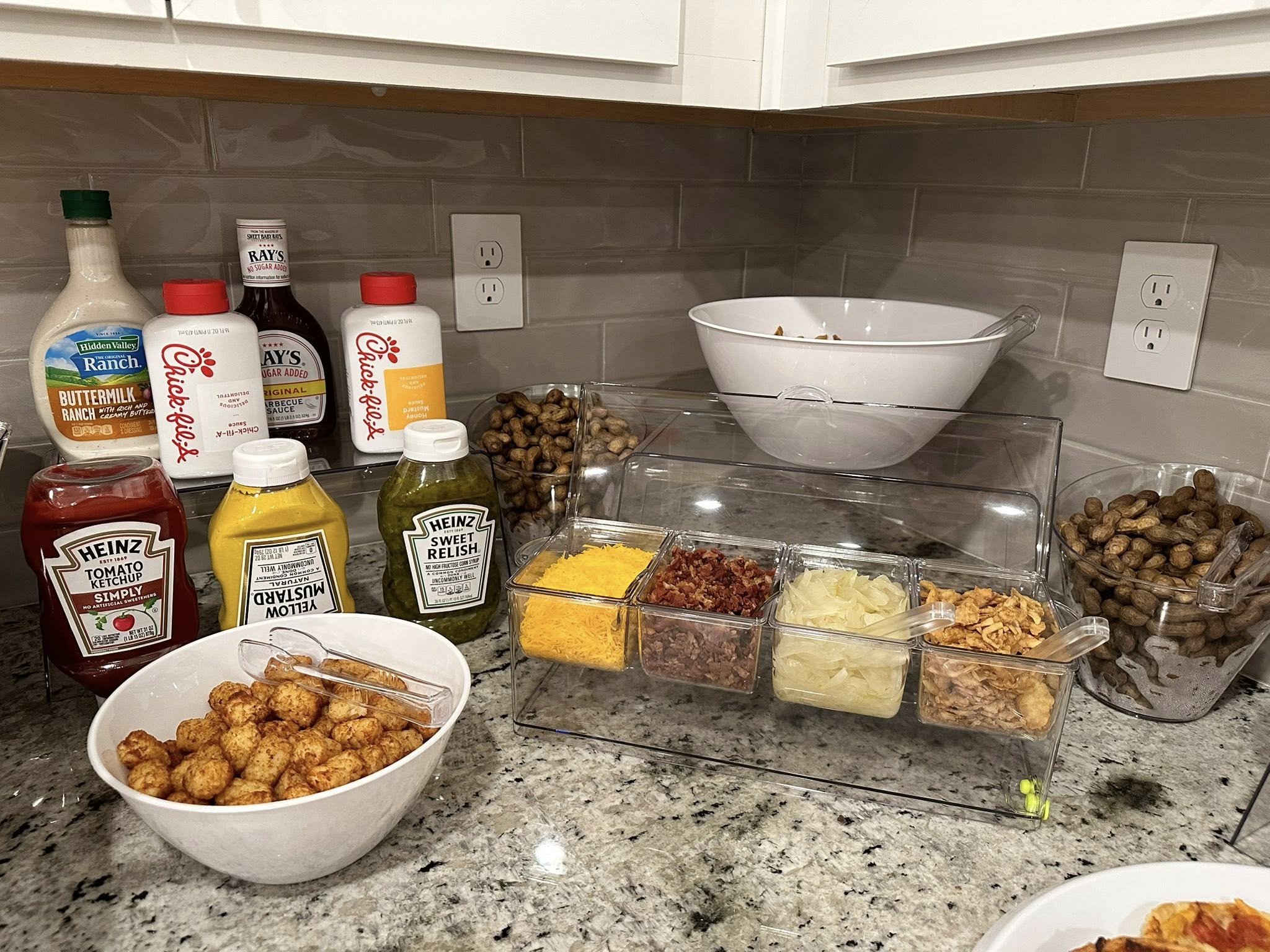 Kitchen counter setup with a condiment garnish station, bowls of tots, and various dipping sauces