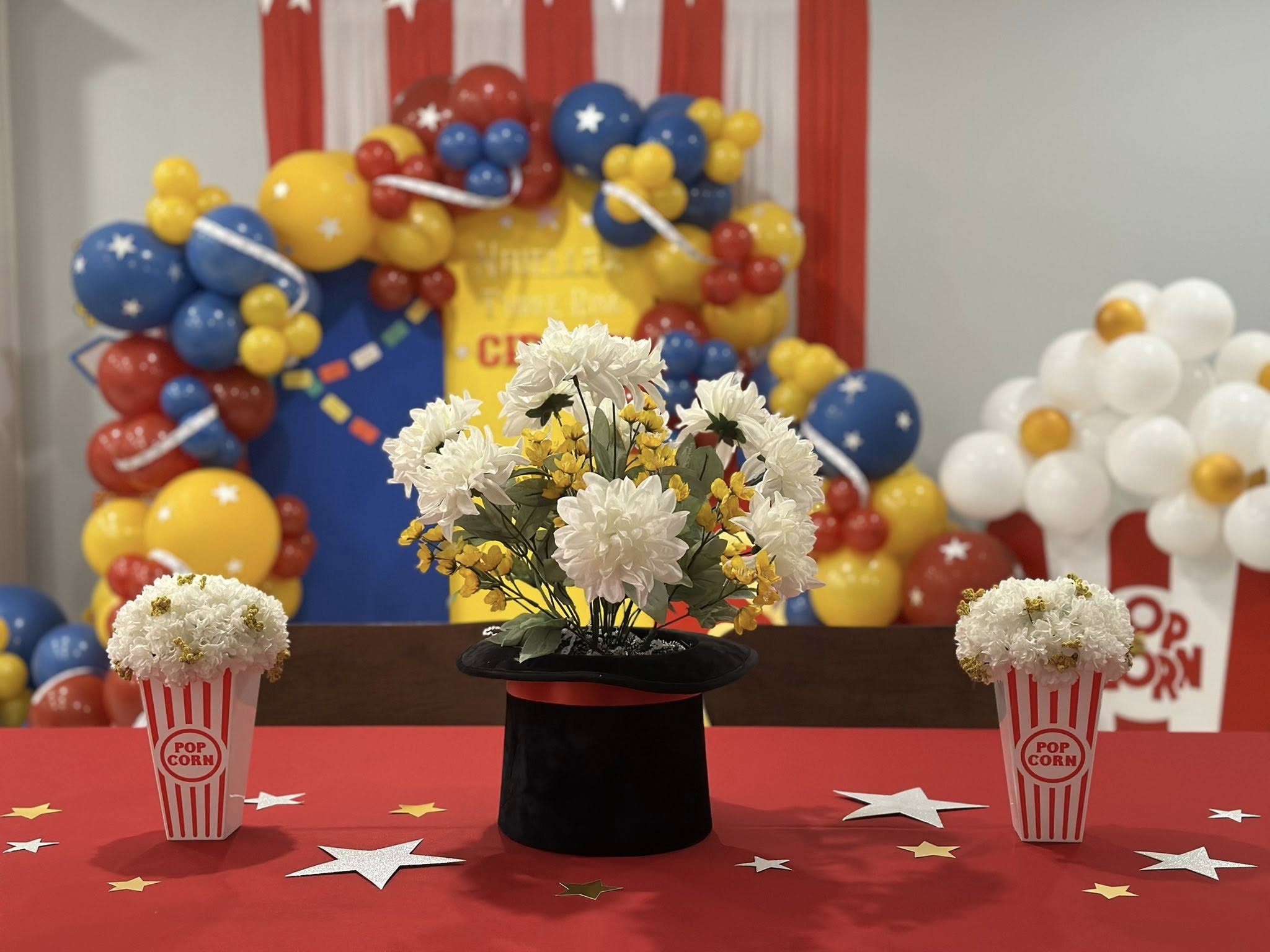 Table centerpiece featuring a bouquet of white and yellow flowers in a black magician hat, flanked by two popcorn boxes.