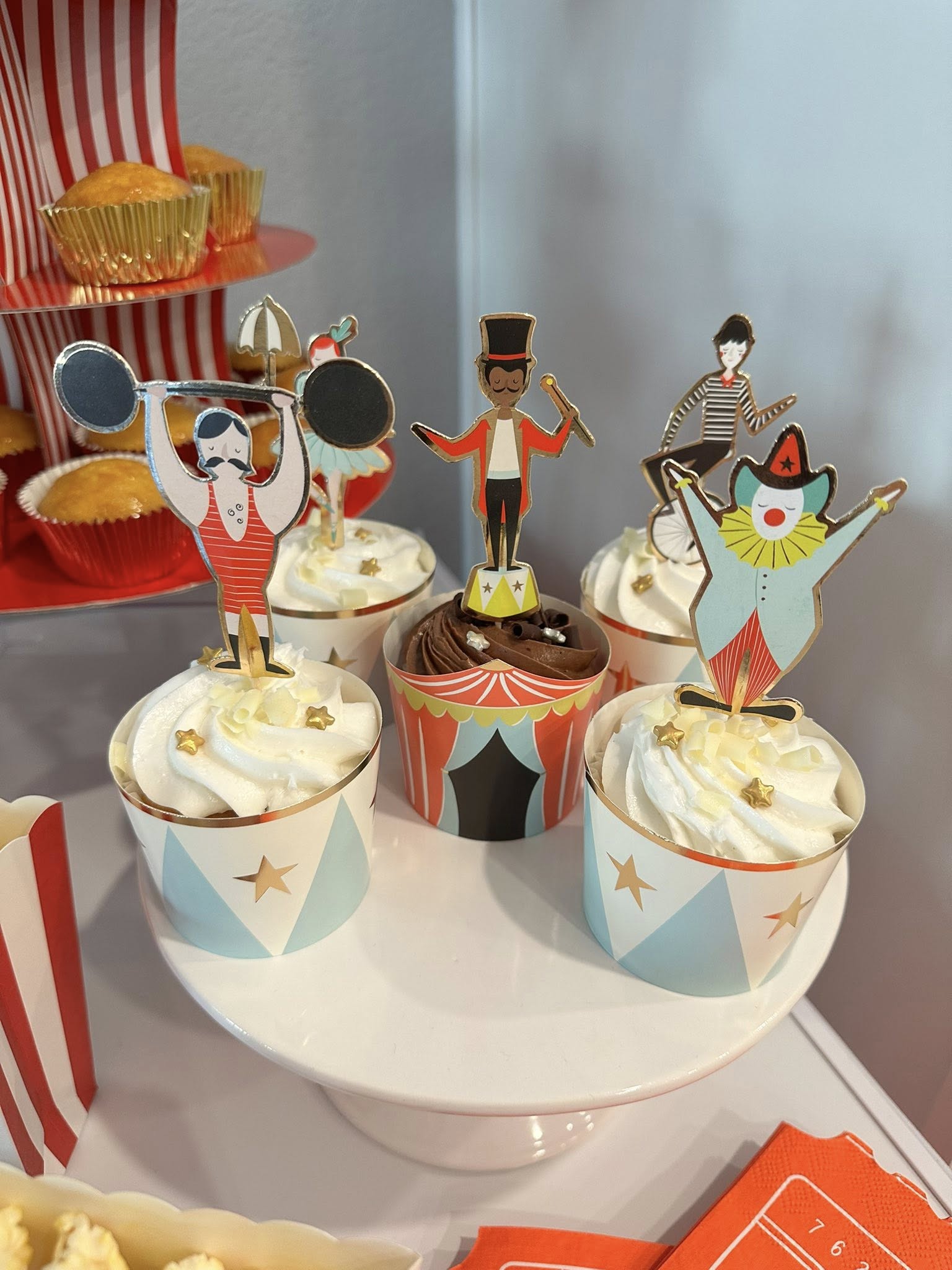 Cupcakes with whimsical circus-themed toppers featuring a strongman, ringmaster, unicyclist, and clown.