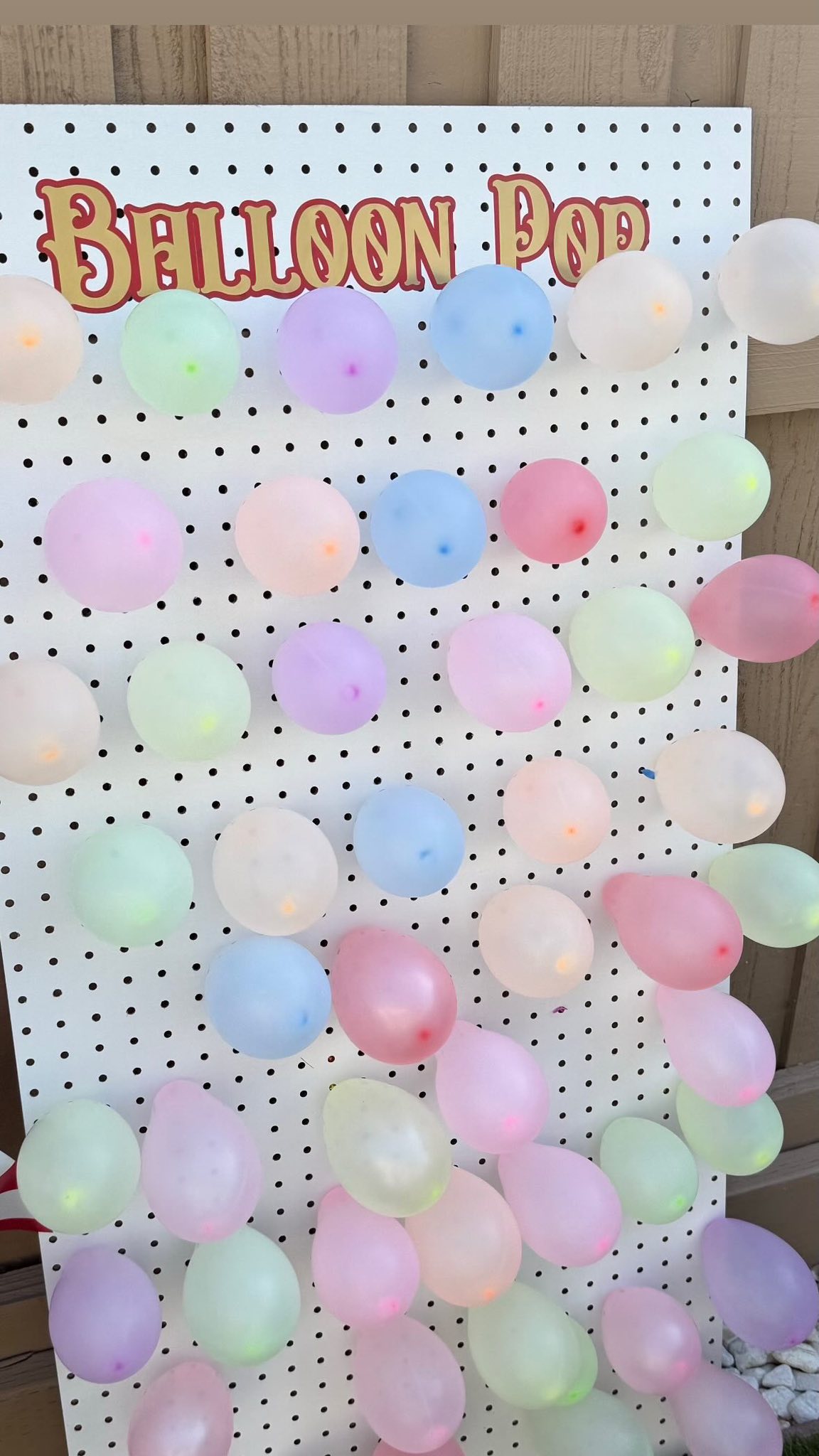 Pegboard game sign for Balloon Pop, pre-filled with assorted pastel-colored balloons.