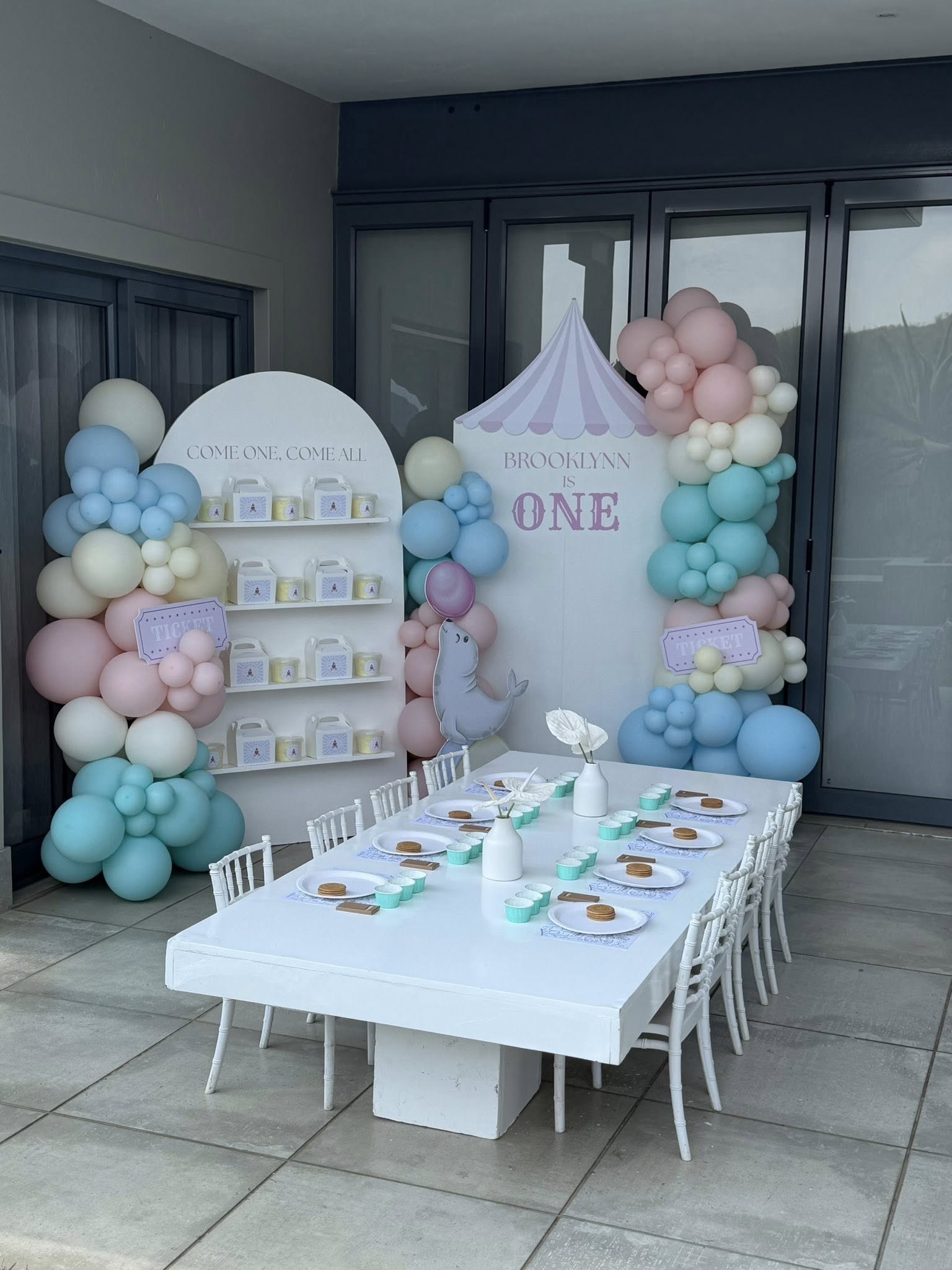 Circus themed first birthday party decor with pastel balloon arches, snack boxes, and a kids table.