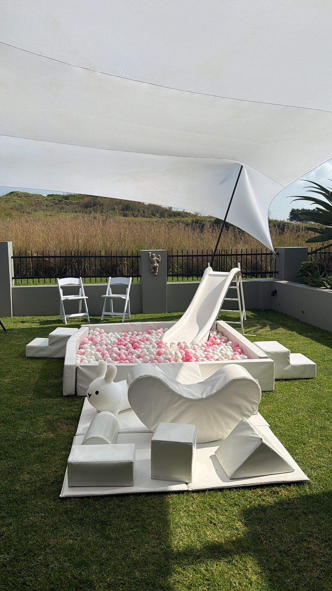 Outdoor soft play set with a white slide, ball pit filled with pink and white balls, foam shapes, and a toy bunny.