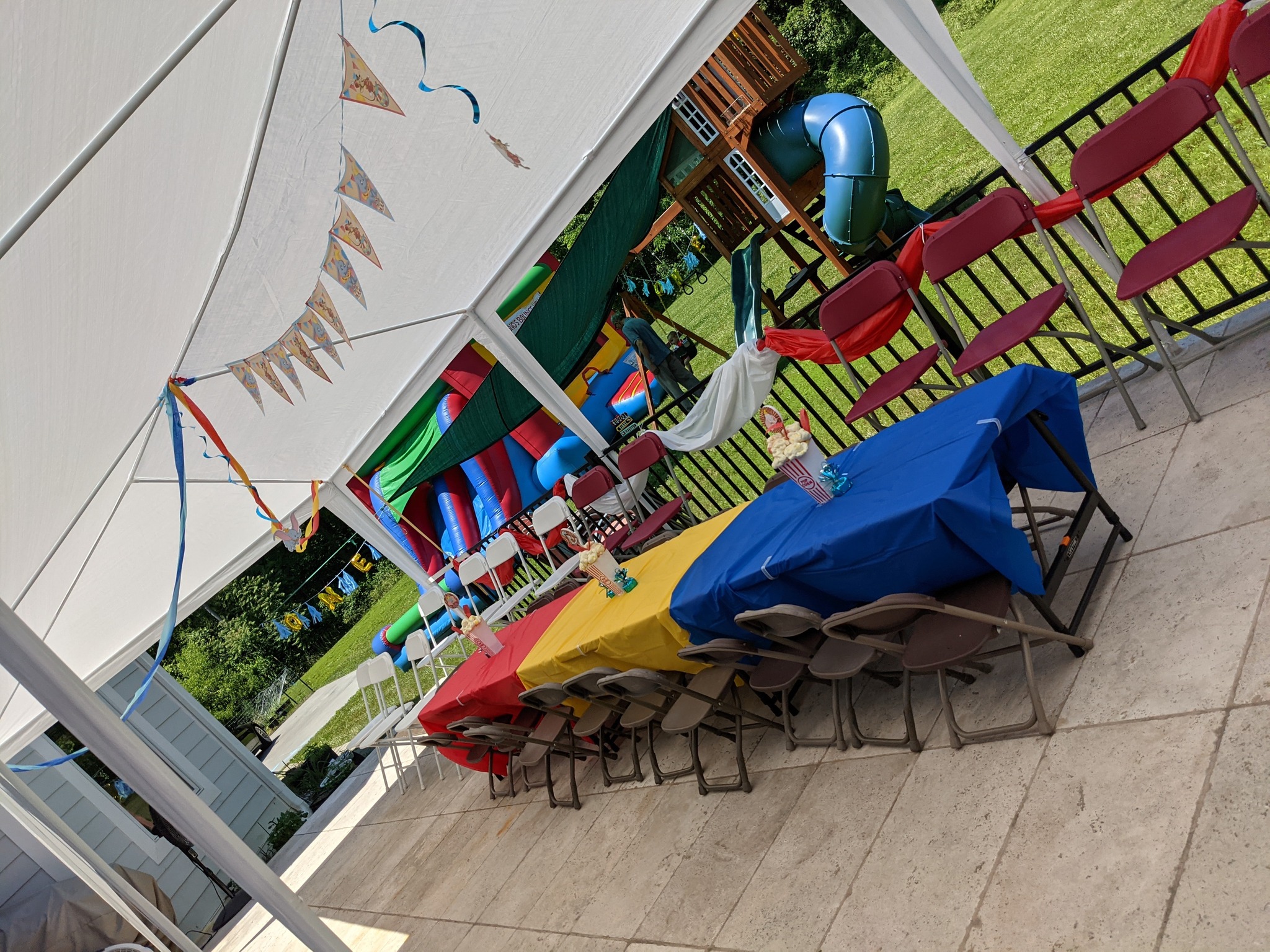 Outdoor party setup with colorful tables under a canopy and a bouncy house in the background