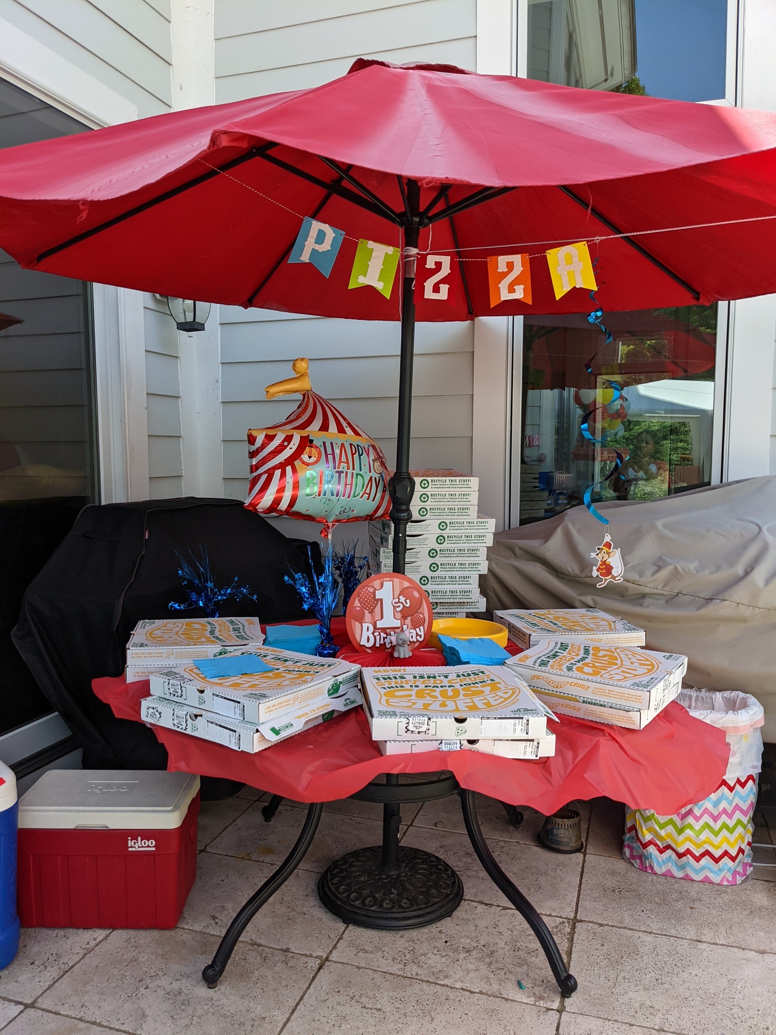 Table set with Papa Johns pizza boxes under a red patio umbrella for a first birthday party.
