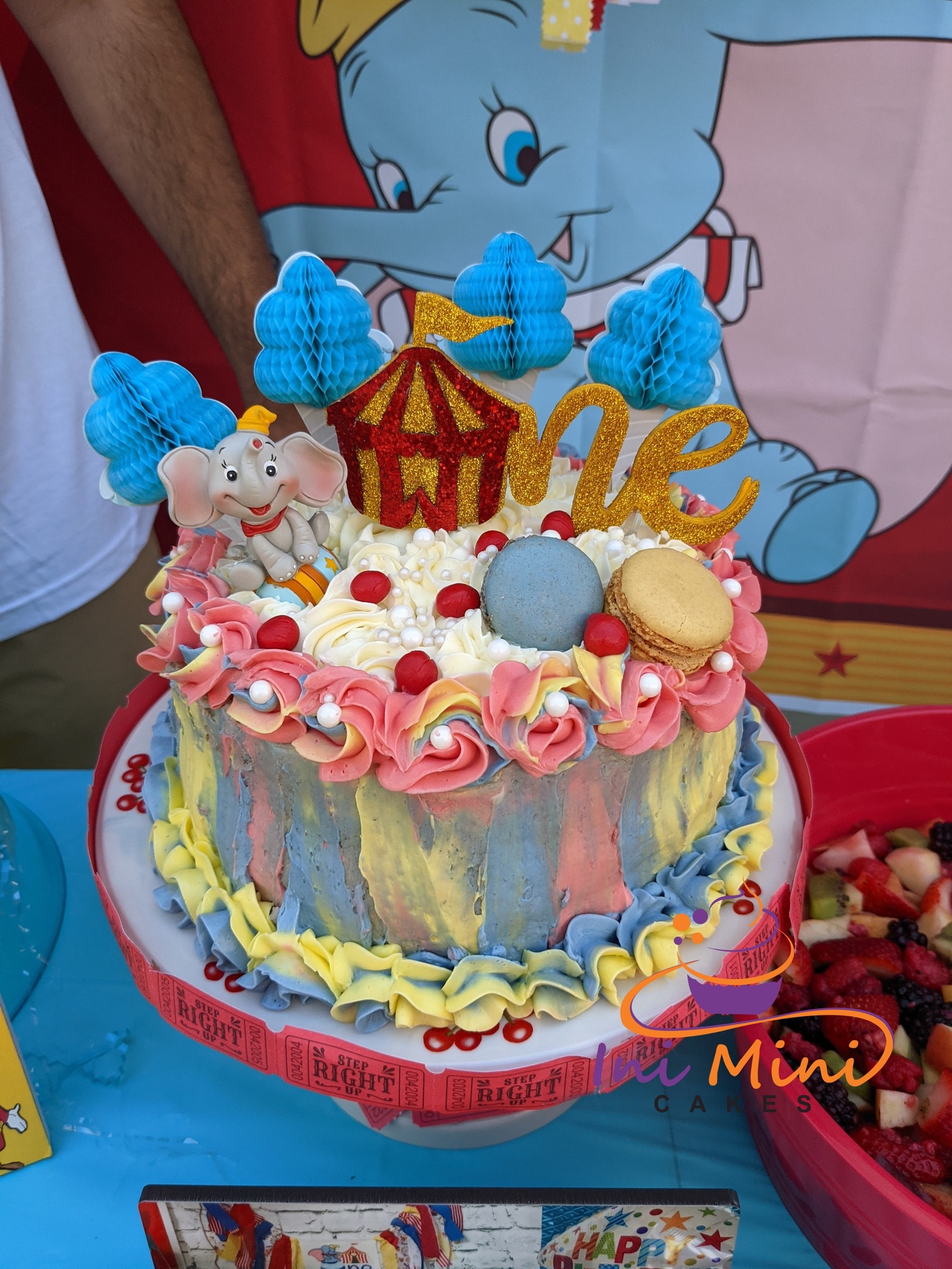 Dumbo-themed first birthday cake with a circus tent topper, blue honeycomb clouds, and buttercream swirls.