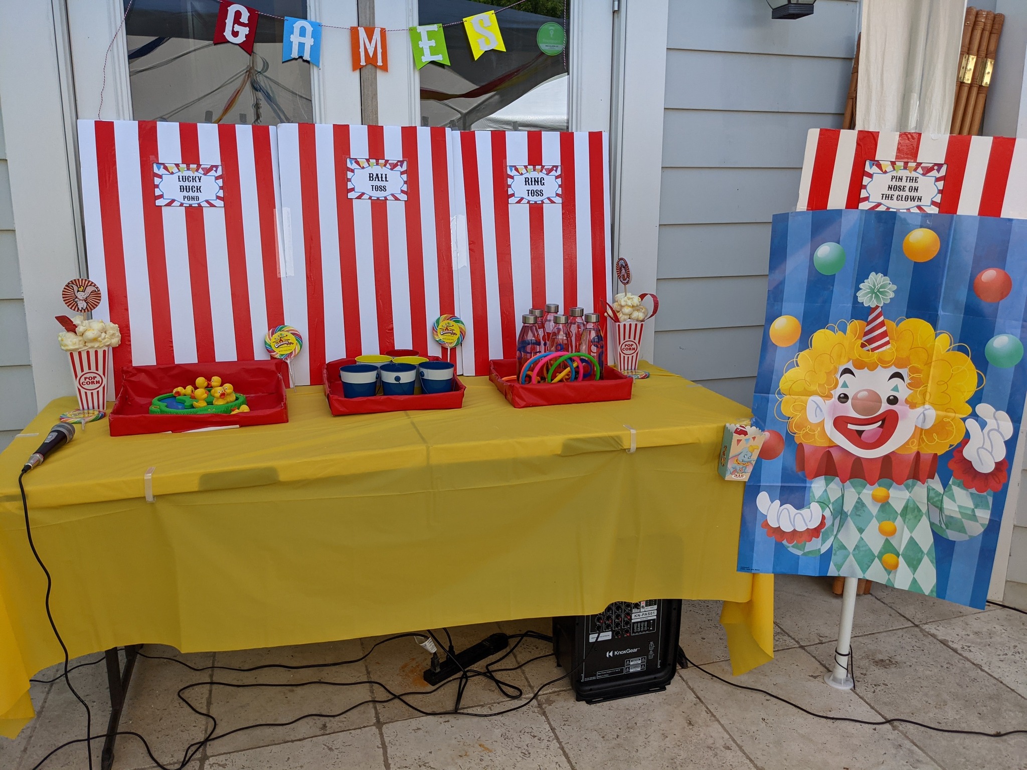Carnival game table setup with lucky duck pond, ball toss, ring toss, and a pin the nose on the clown game.