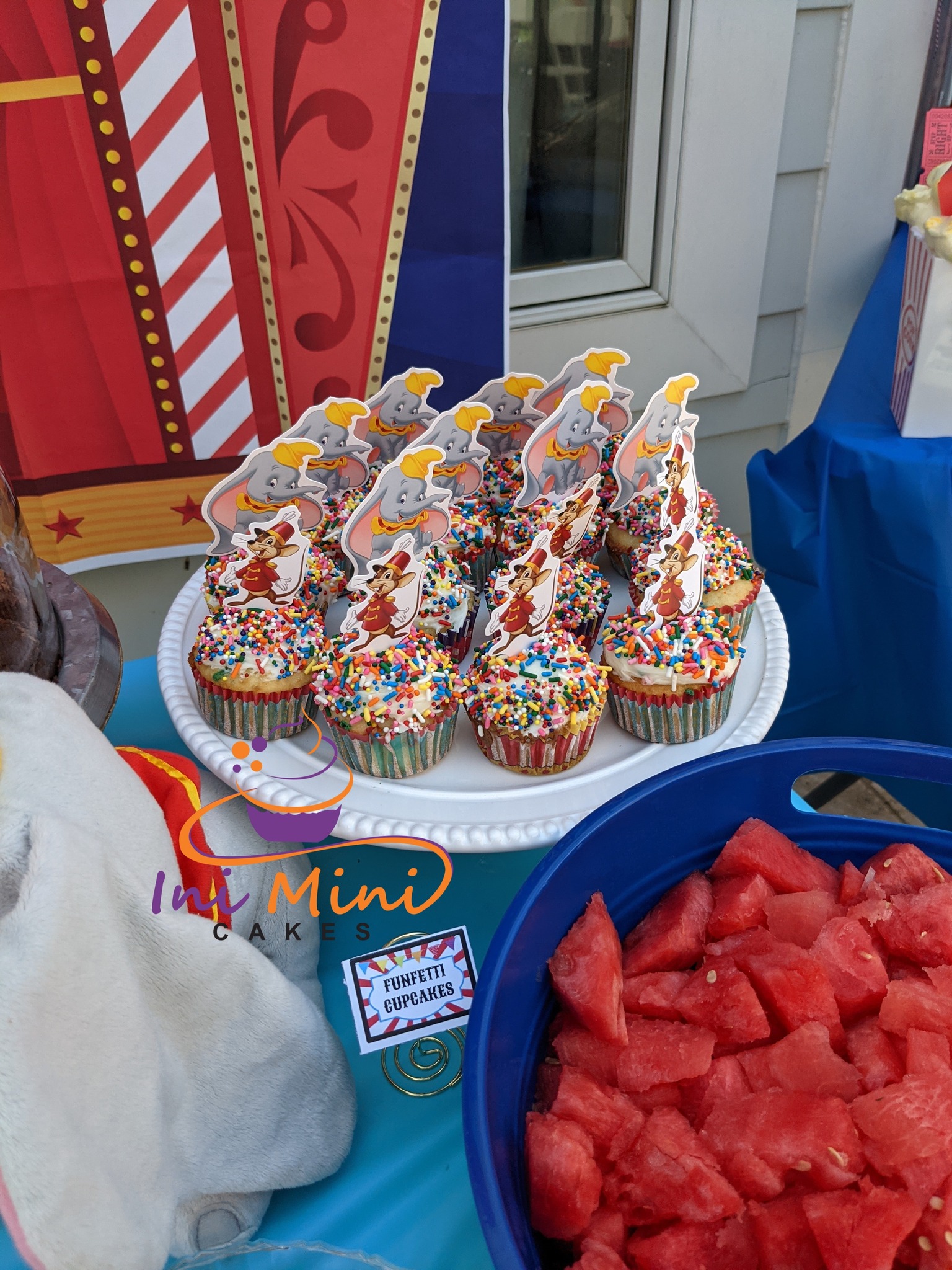 Dumbo themed funfetti cupcakes topped with character cupcake toppers on a white platter at a carnival party.