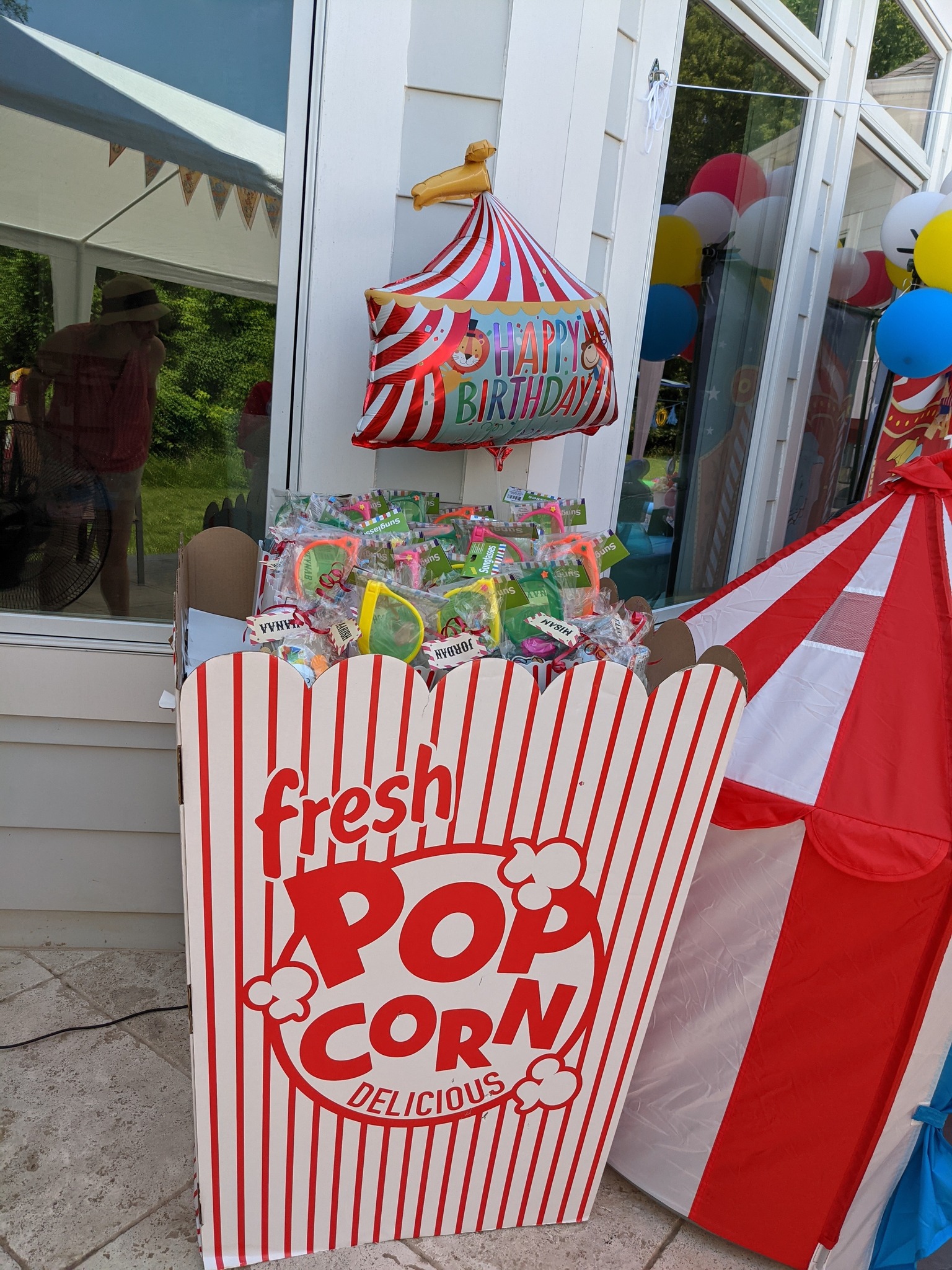 Popcorn-themed cardboard favor station filled with individually wrapped party sunglasses at a circus-themed party.