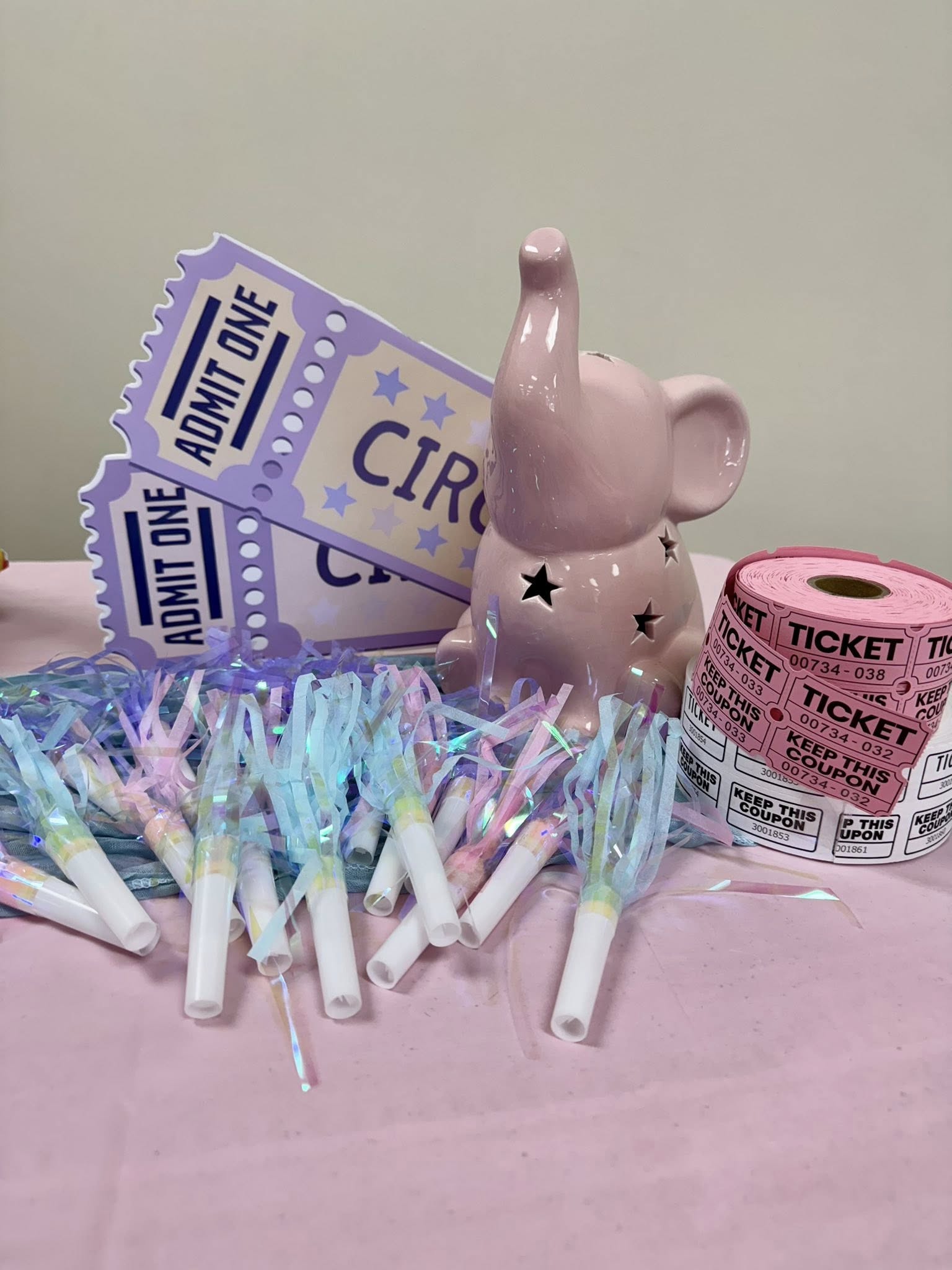 Table setting with circus tickets, pink ceramic elephant, and iridescent party blowers.