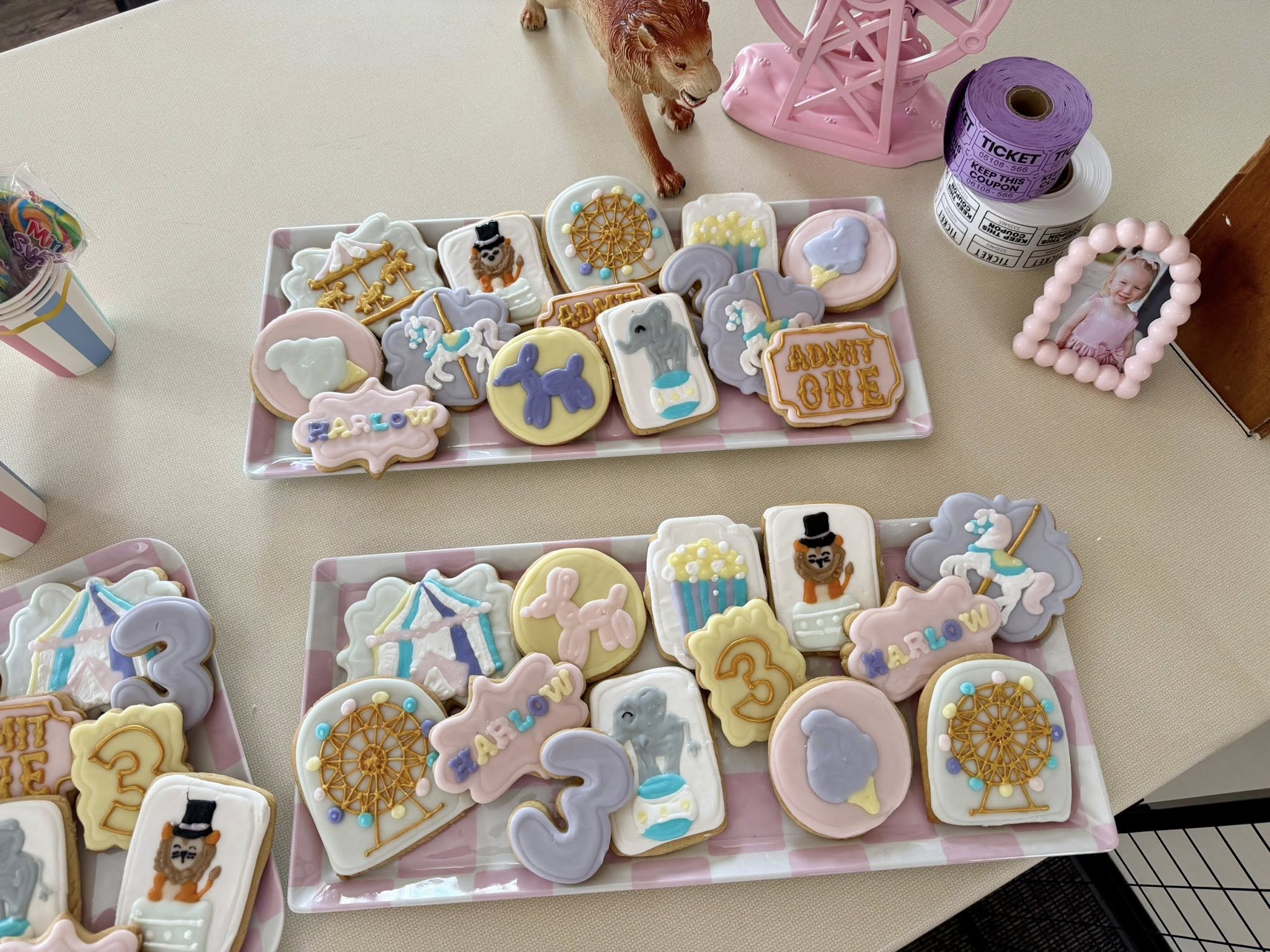 Platters of custom decorated carnival-themed sugar cookies featuring Ferris wheels, circus animals, and number three shapes.