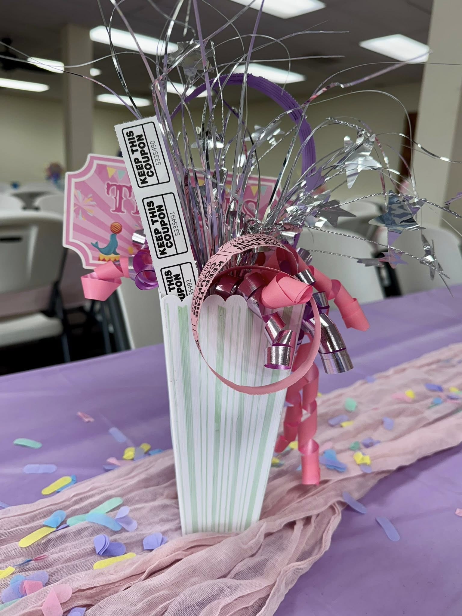 Carnival-themed centerpiece with a popcorn box, raffle tickets, and metallic star sprays on a table