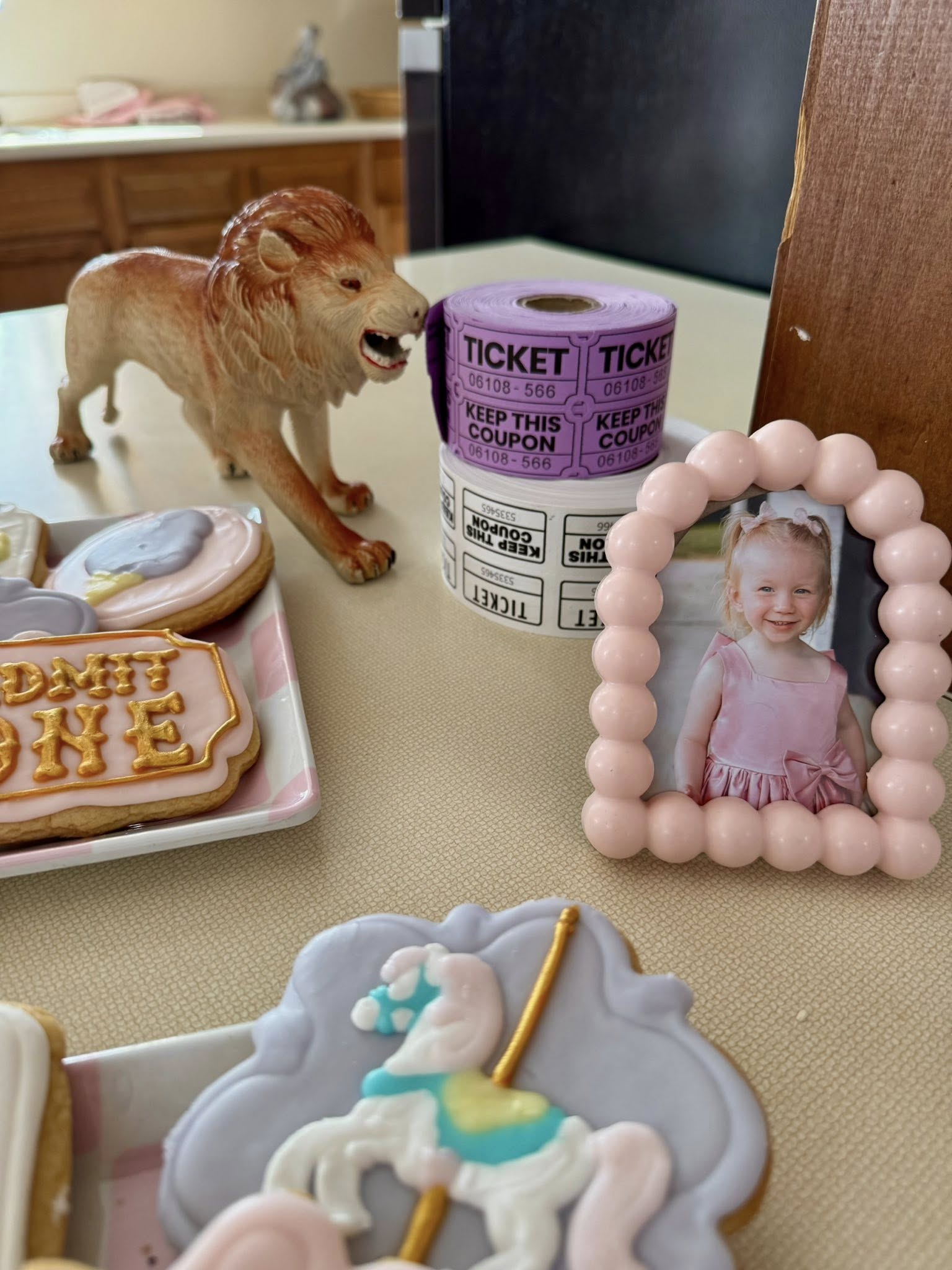 Circus-themed party table decorations including Admit One cookies, a lion figurine, admission tickets, and a photo.