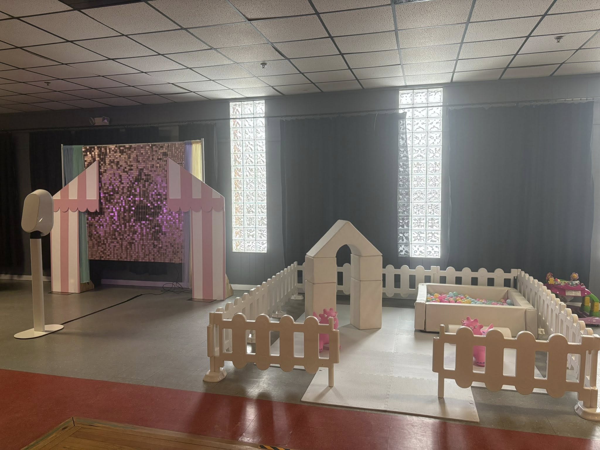 Indoor soft play area featuring a white fence, foam climbing blocks, and a small ball pit with pink toys.