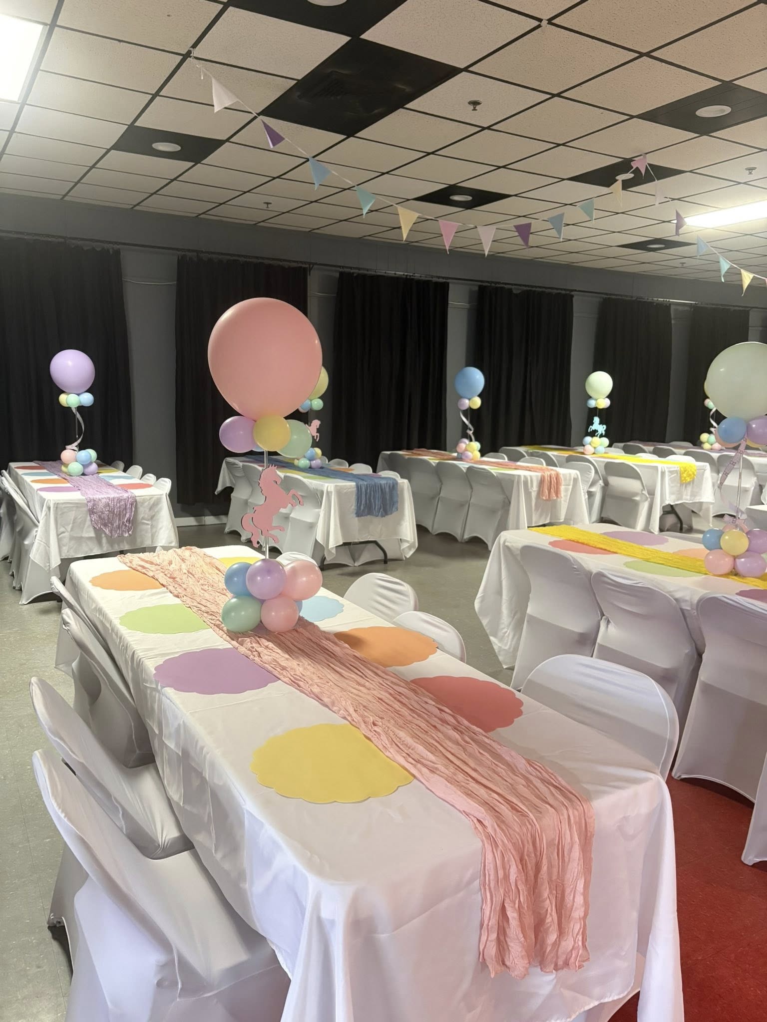 Room set up for a unicorn themed party with pastel balloon centerpieces and colorful table runners