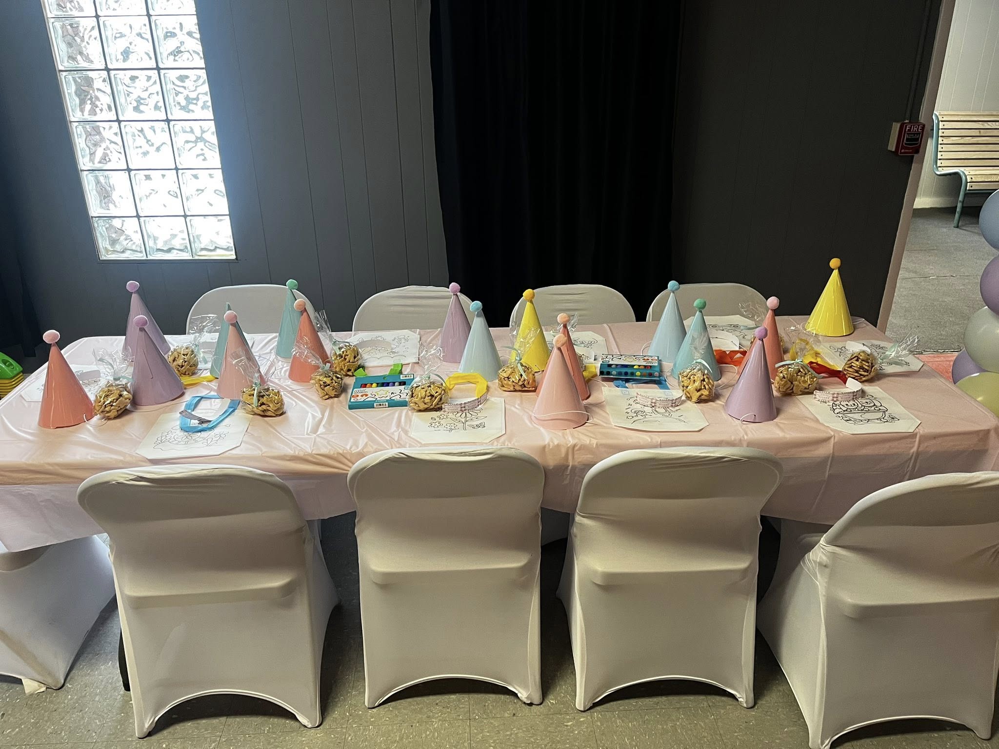 Party table set for a birthday with colorful hats, snacks, and art activity sheets at each place setting.
