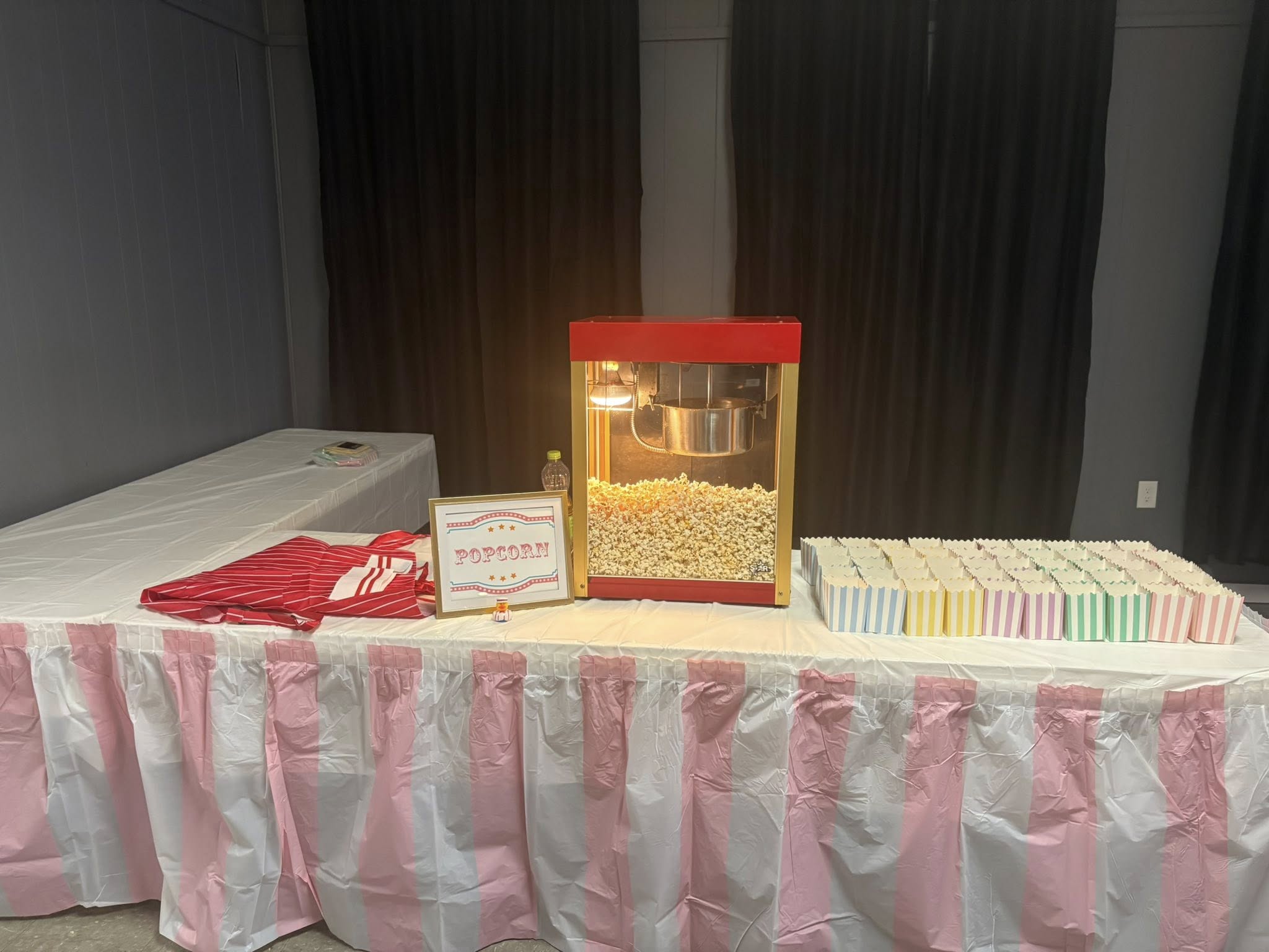 Popcorn machine on a table with a sign and striped serving containers for a party