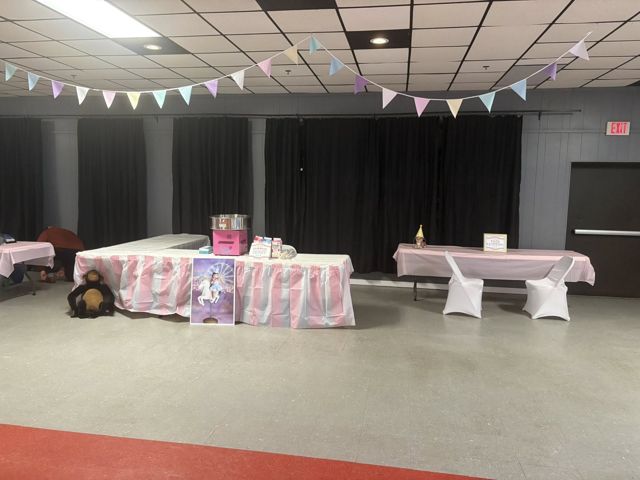 Carnival-themed event setup with a cotton candy machine, pink and white table skirts, and party bunting decor.