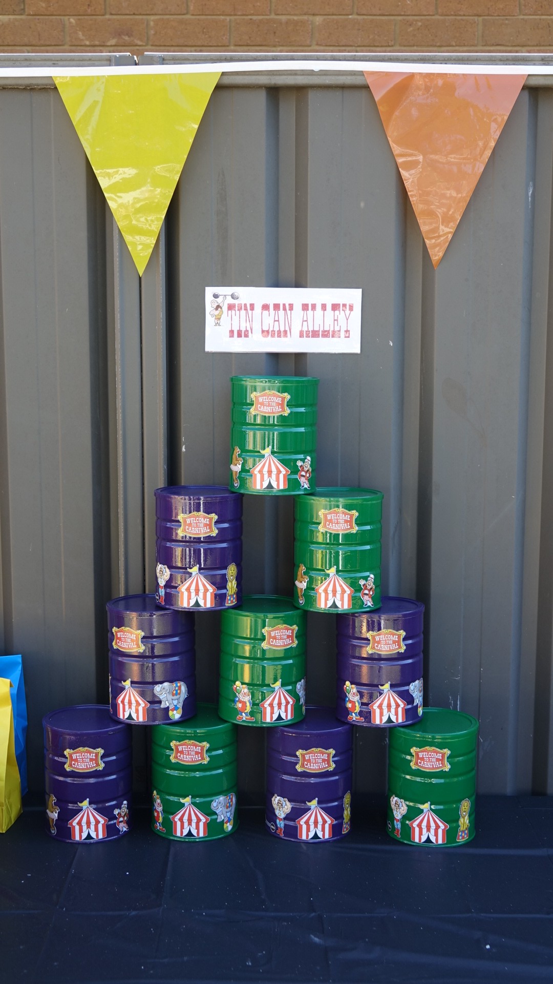 Tin Can Alley carnival game with stacked green and purple cans labeled Welcome to the Carnival.