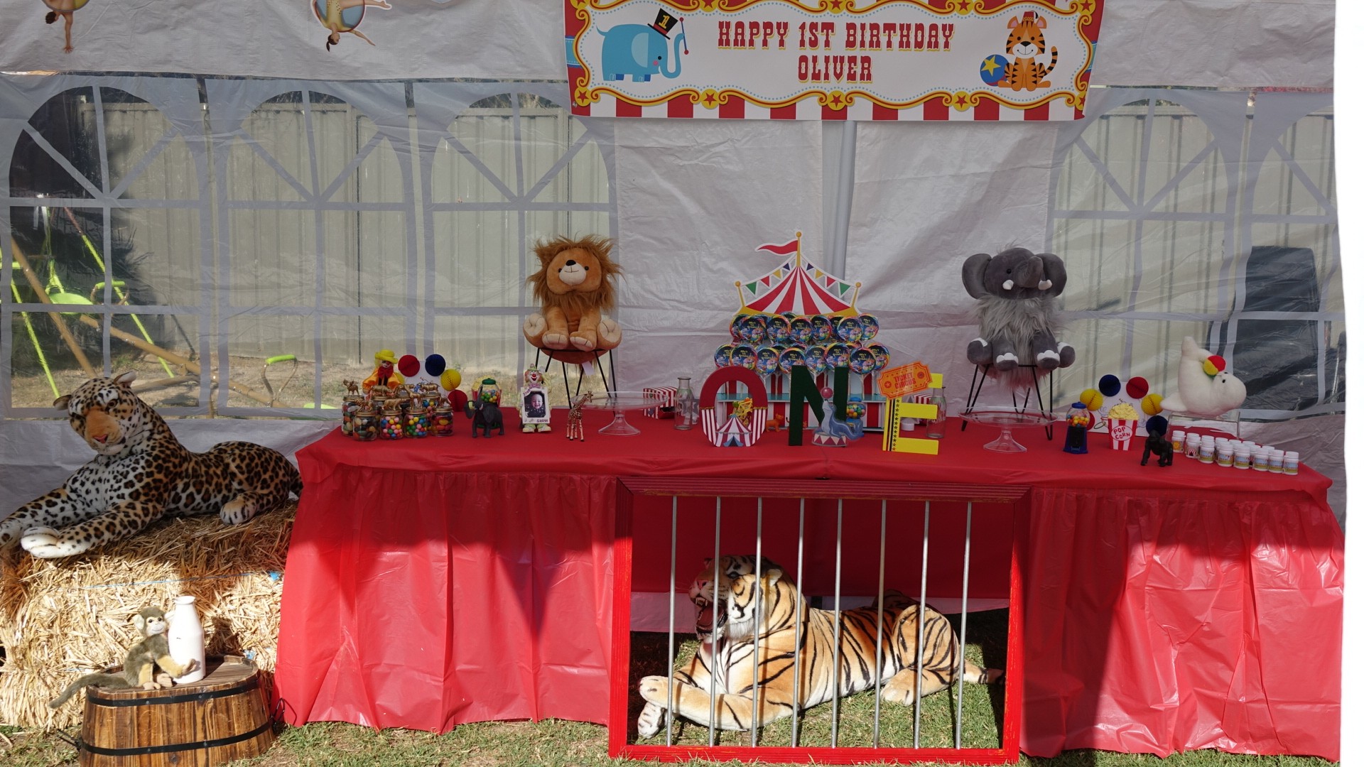 Carnival-themed dessert table for a first birthday party with plush circus animals, red table skirt, and tiger prop