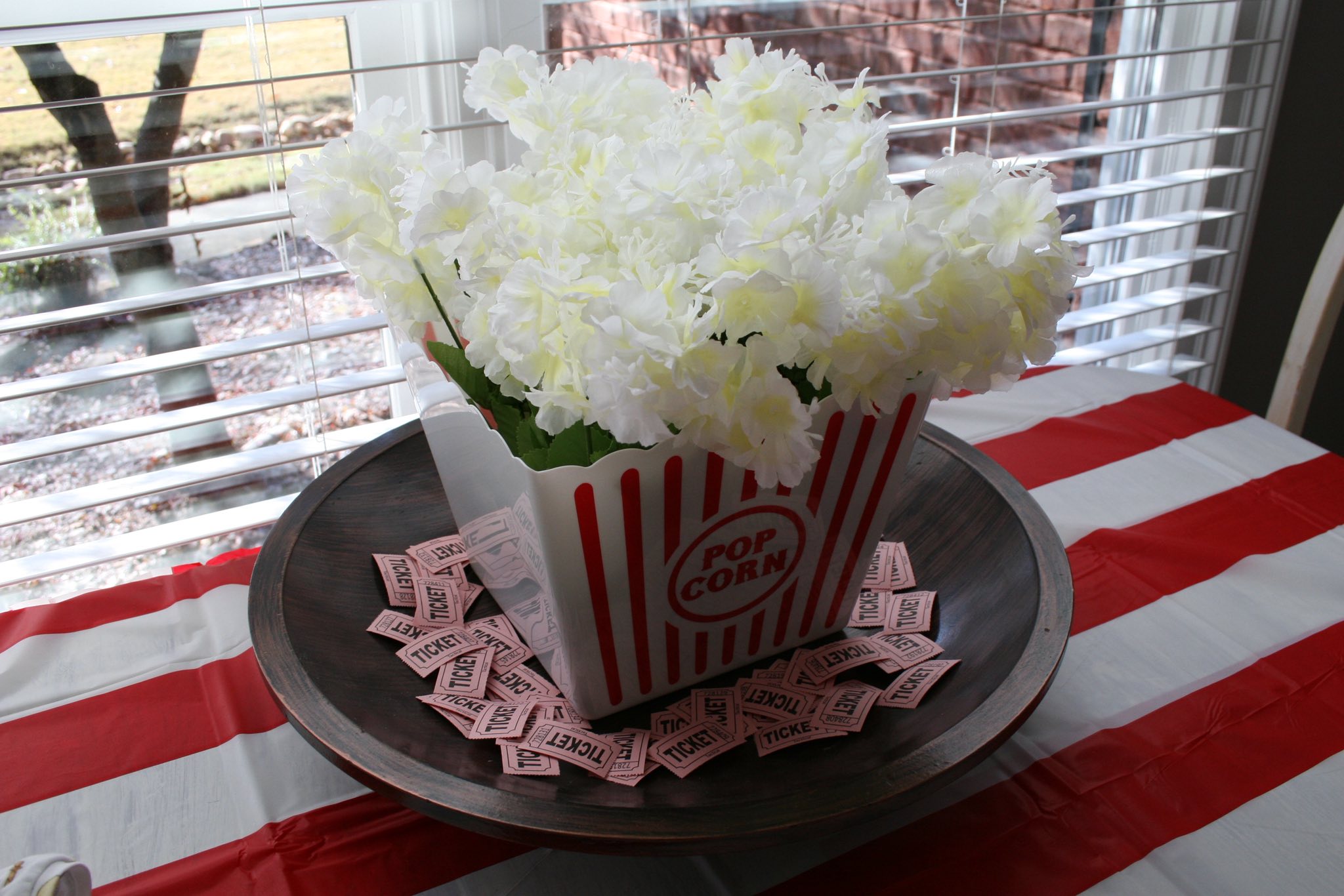 Popcorn container centerpiece filled with white flowers and surrounded by movie tickets on a rustic tray