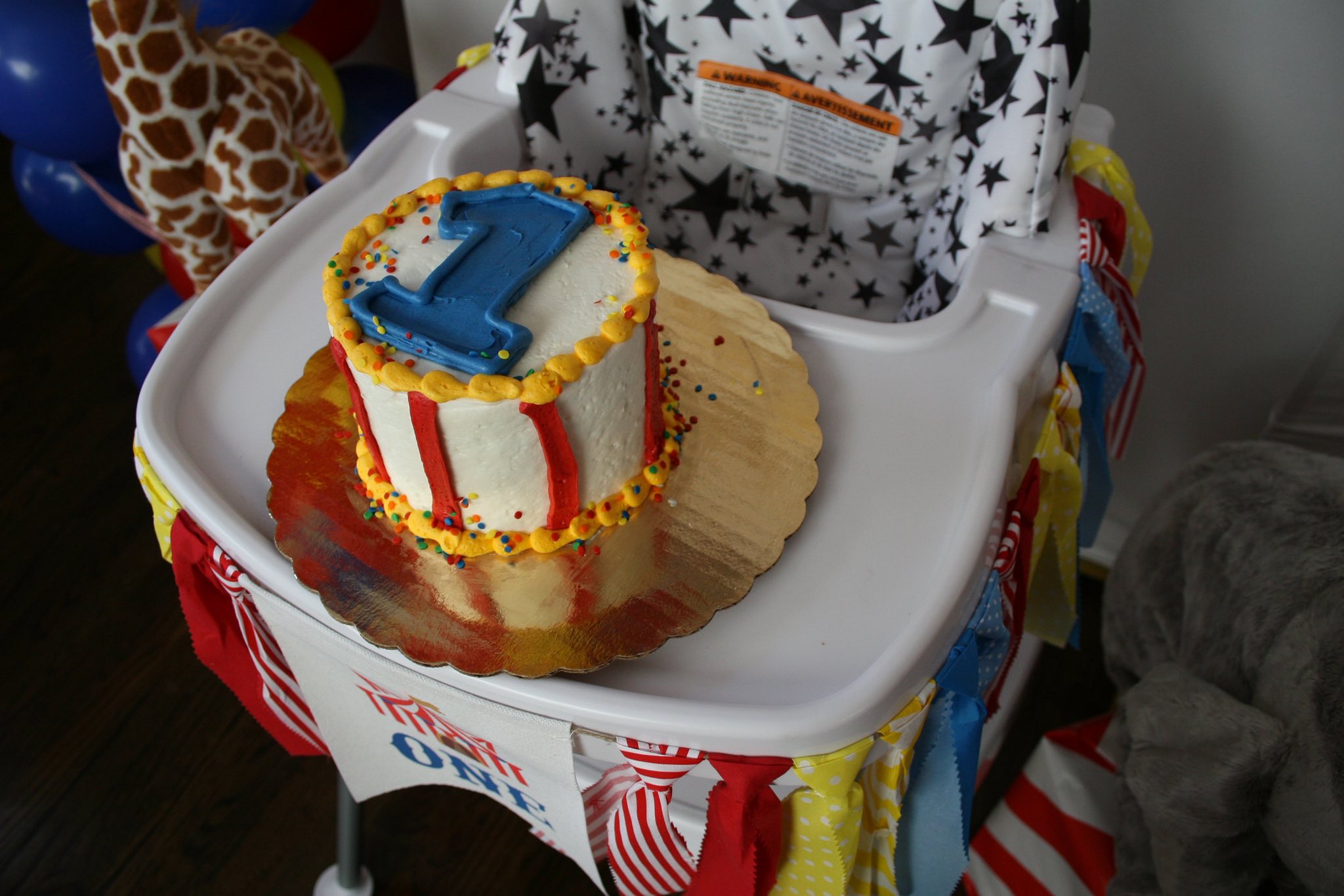 Small round first birthday cake with white frosting and a blue number one topper on a high chair tray