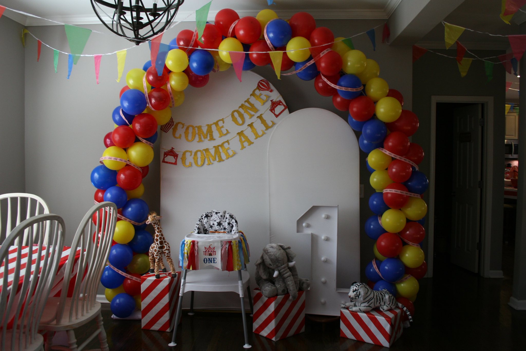 First birthday party decoration with a colorful balloon arch, a number one prop, and carnival-themed stuffed animals.