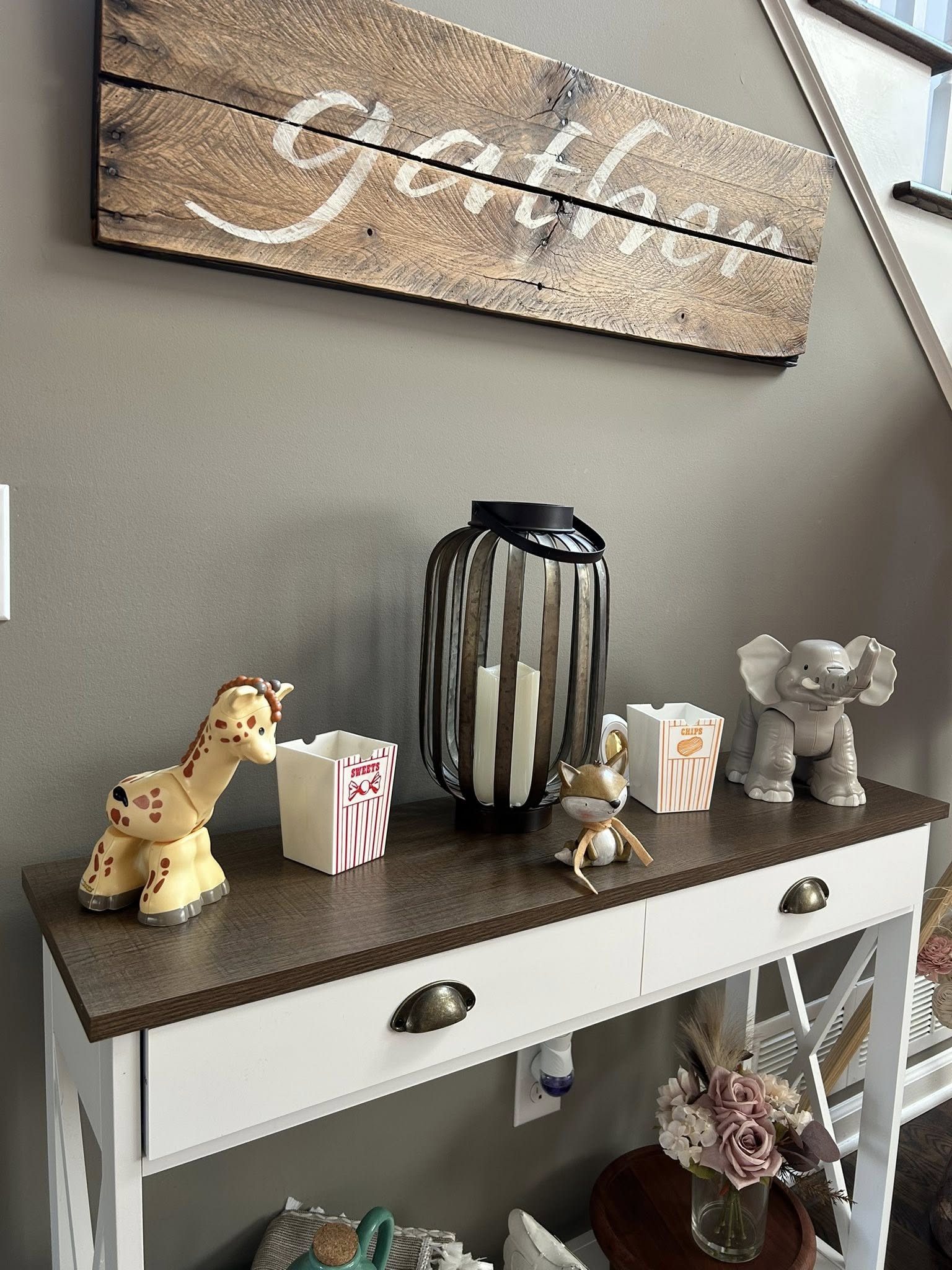 Tabletop console table decorated with a wooden Gather sign, a lantern, and animal figurines.