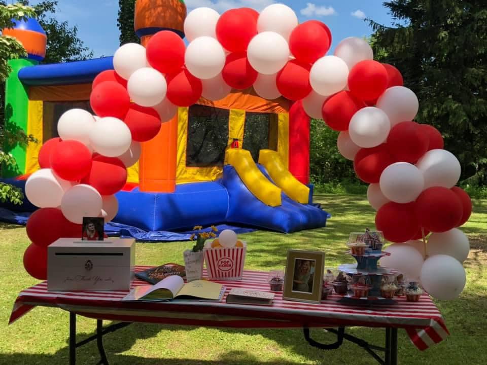Red and white balloon arch over a party table with bounce house in background
