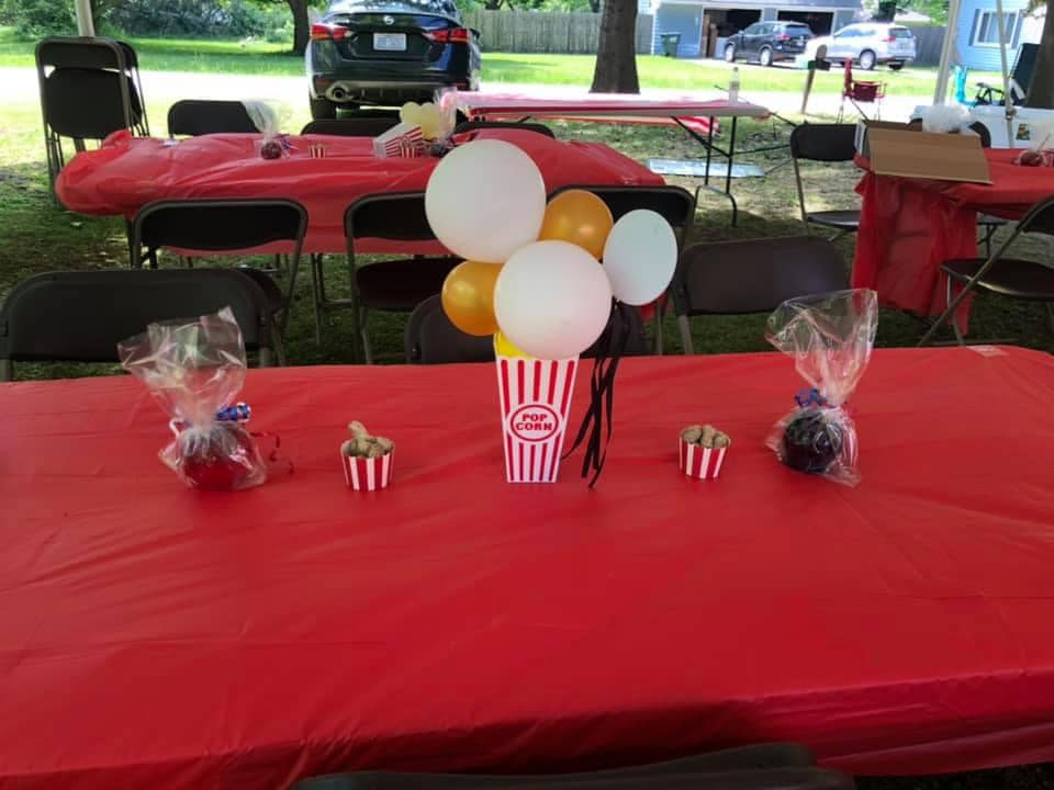 Event table with red tablecloth, popcorn box balloon centerpiece, and wrapped treats.
