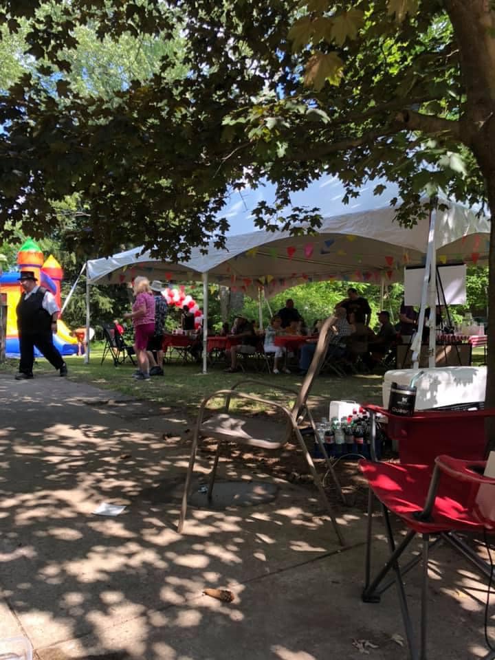 People gathering under a party tent at an outdoor community event with an inflatable bounce house nearby.