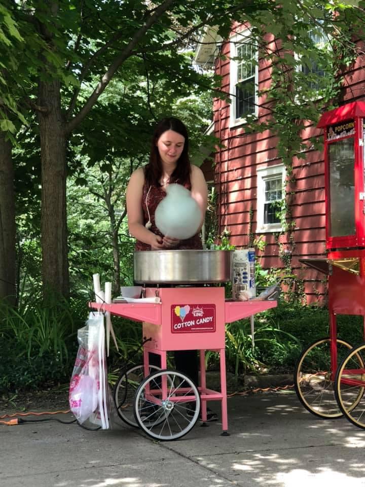 Woman preparing fresh blue cotton candy at a pink portable carnival-style cotton candy machine