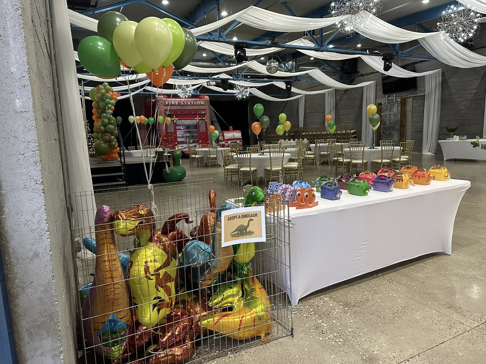 Adopt-a-dinosaur booth with metallic dinosaur balloons in a cage and colorful party favor boxes on a table.