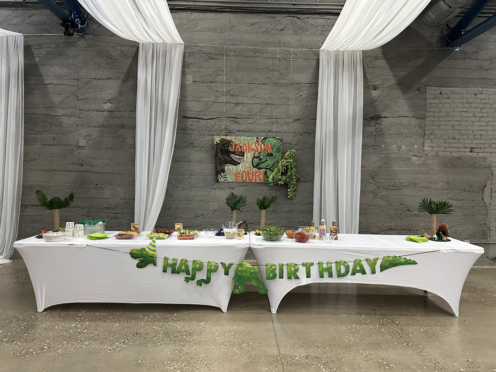 Dinosaur themed birthday party food table decorated with a Happy Birthday banner and custom sign.