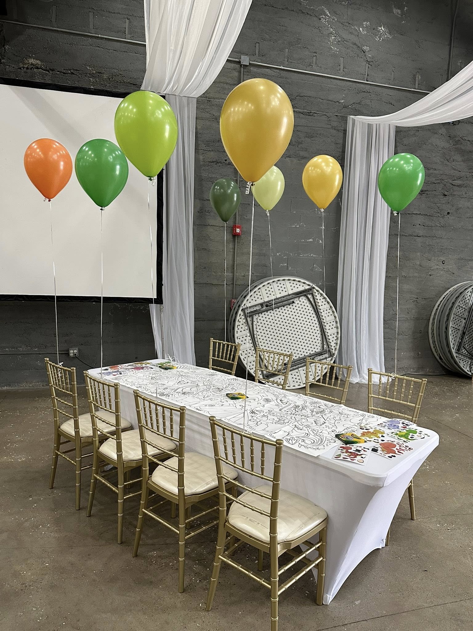 Table set up for children with coloring paper and crayons, decorated with green, yellow, and orange balloons.