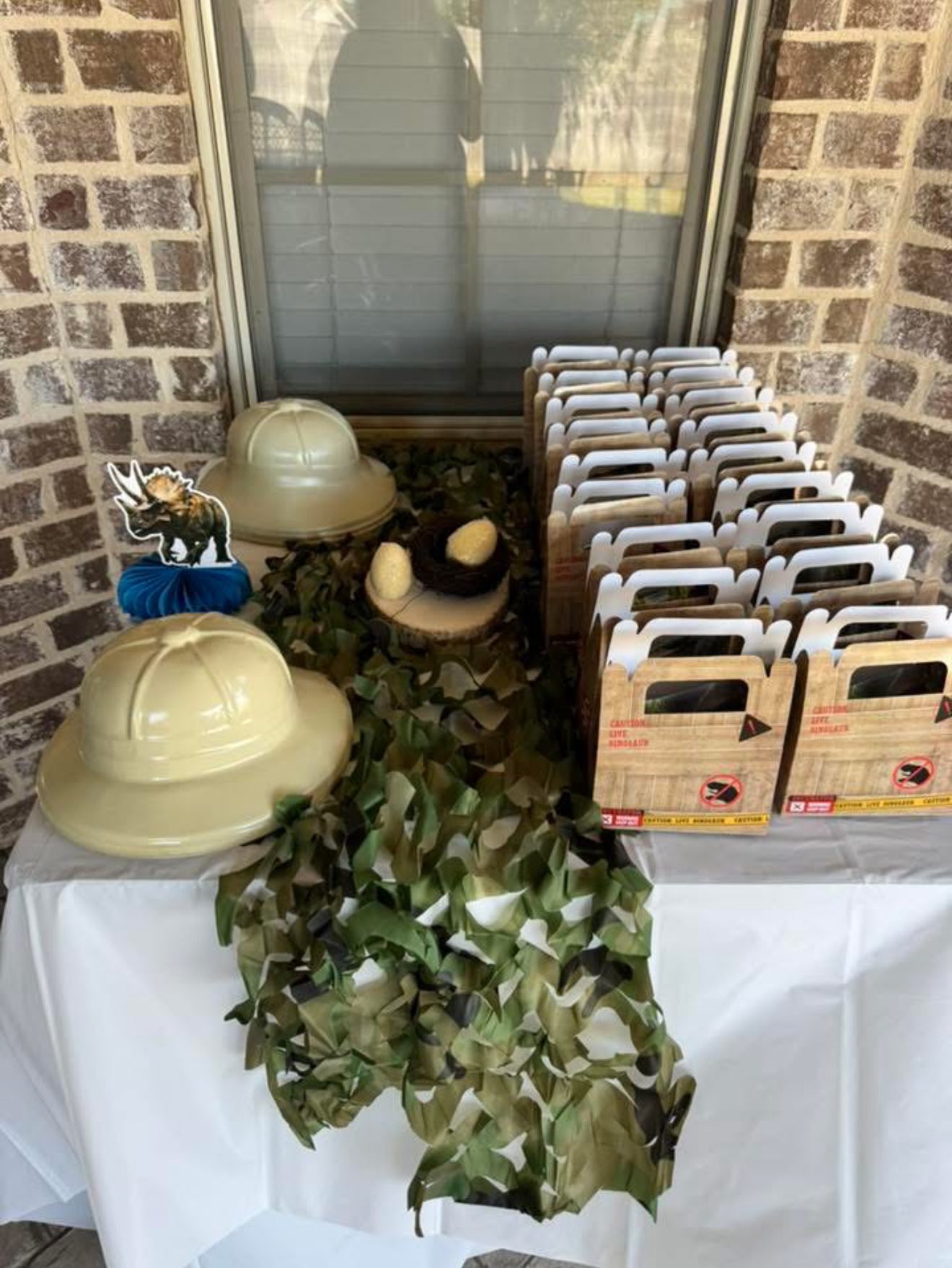 Dinosaur themed party table decorations including safari hats, toy eggs in a nest, and caution crate favor boxes.