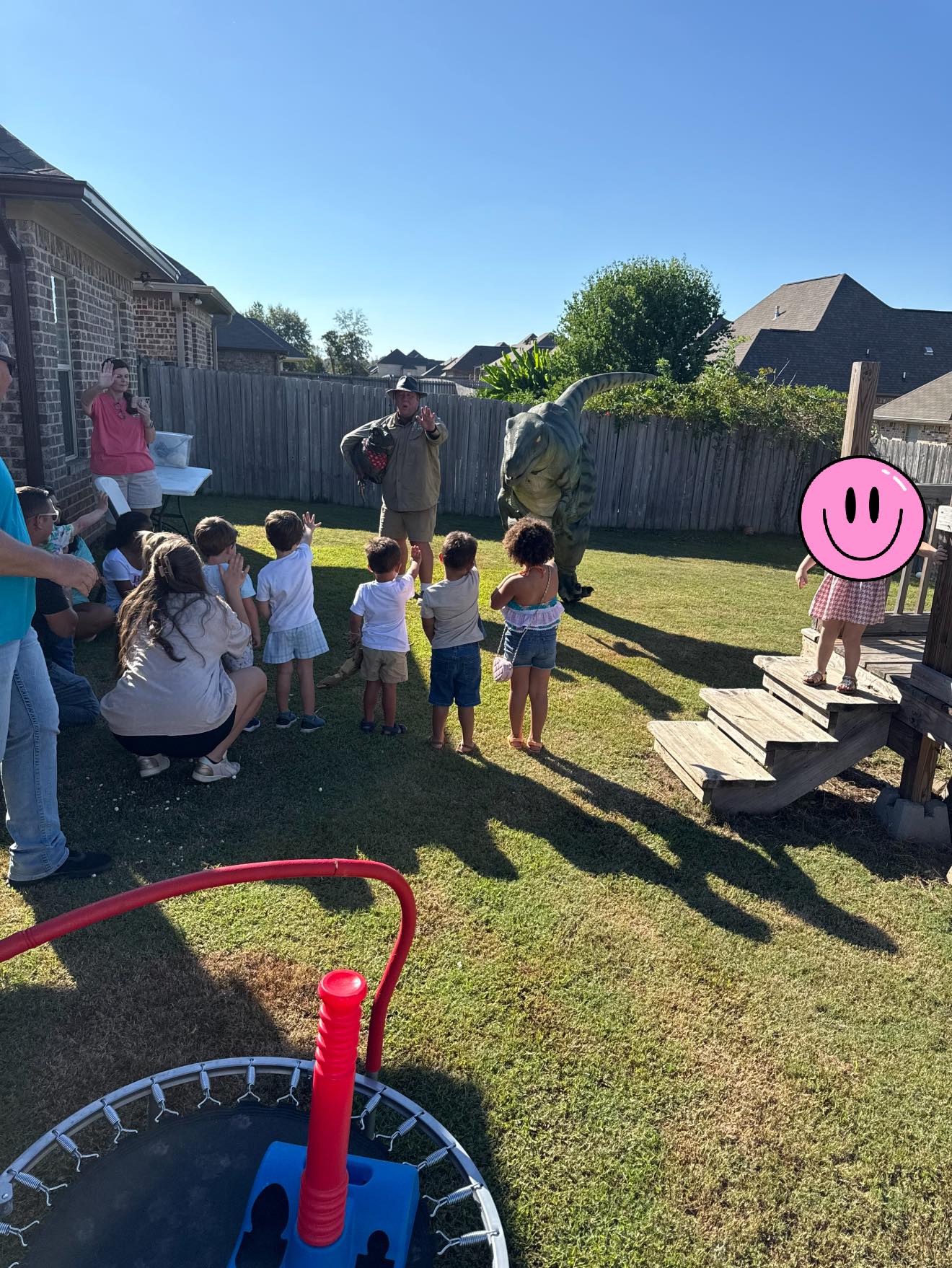 Children participating in an outdoor dinosaur show with a costumed performer in a backyard.