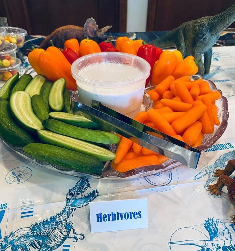 Veggie platter labeled as Herbivores featuring cucumbers, carrots, and peppers on a dinosaur-themed party table.