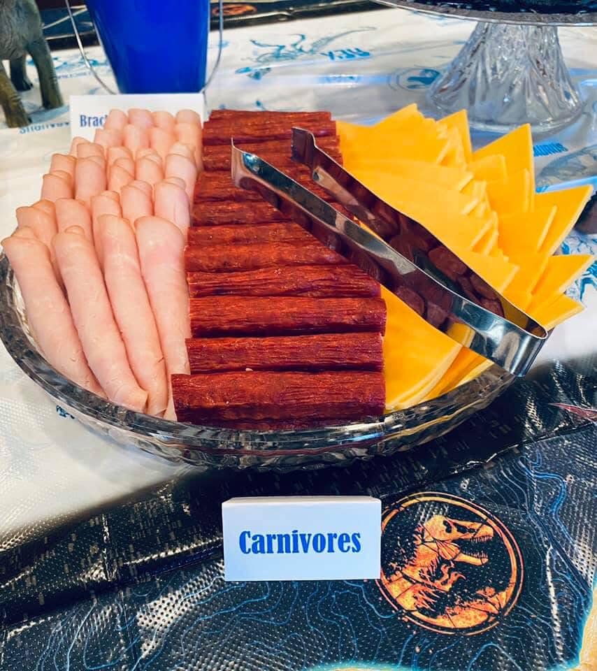 Serving platter with turkey, pepperoni, and cheese slices labeled as a Carnivores dinosaur-themed party snack.