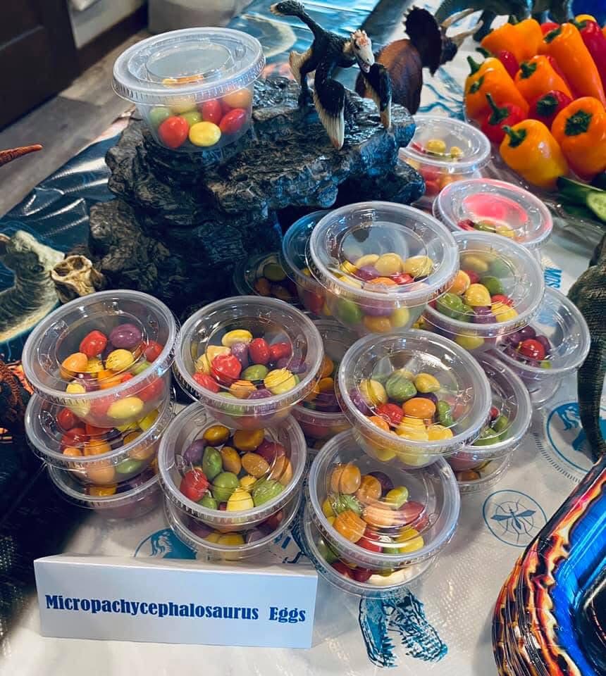 Table display featuring small clear cups filled with colorful candy labeled as Micropachycephalosaurus eggs.
