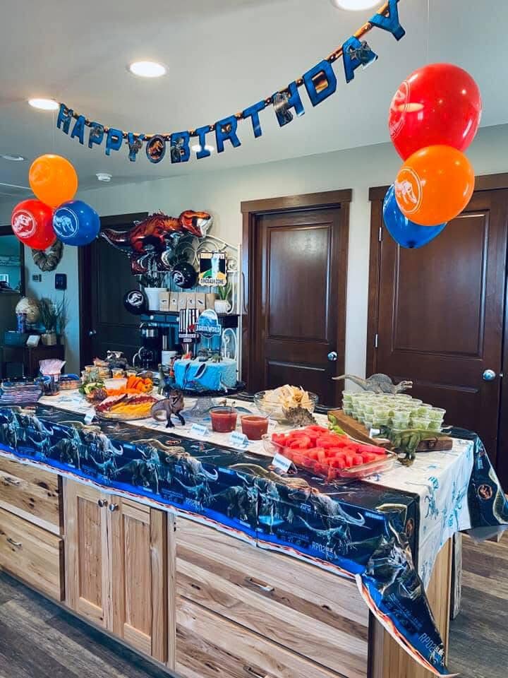 Jurassic World themed birthday party table with dinosaur decorations, balloons, and snacks.