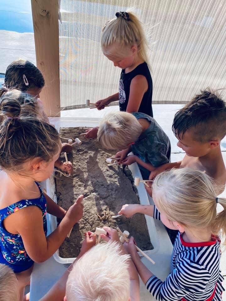 Group of children using small wooden mallets to excavate a dirt-filled sensory bin.