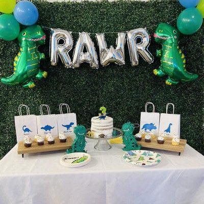Dinosaur themed birthday party setup with RAWR balloon banner, green dinosaur foil balloons, and treats.
