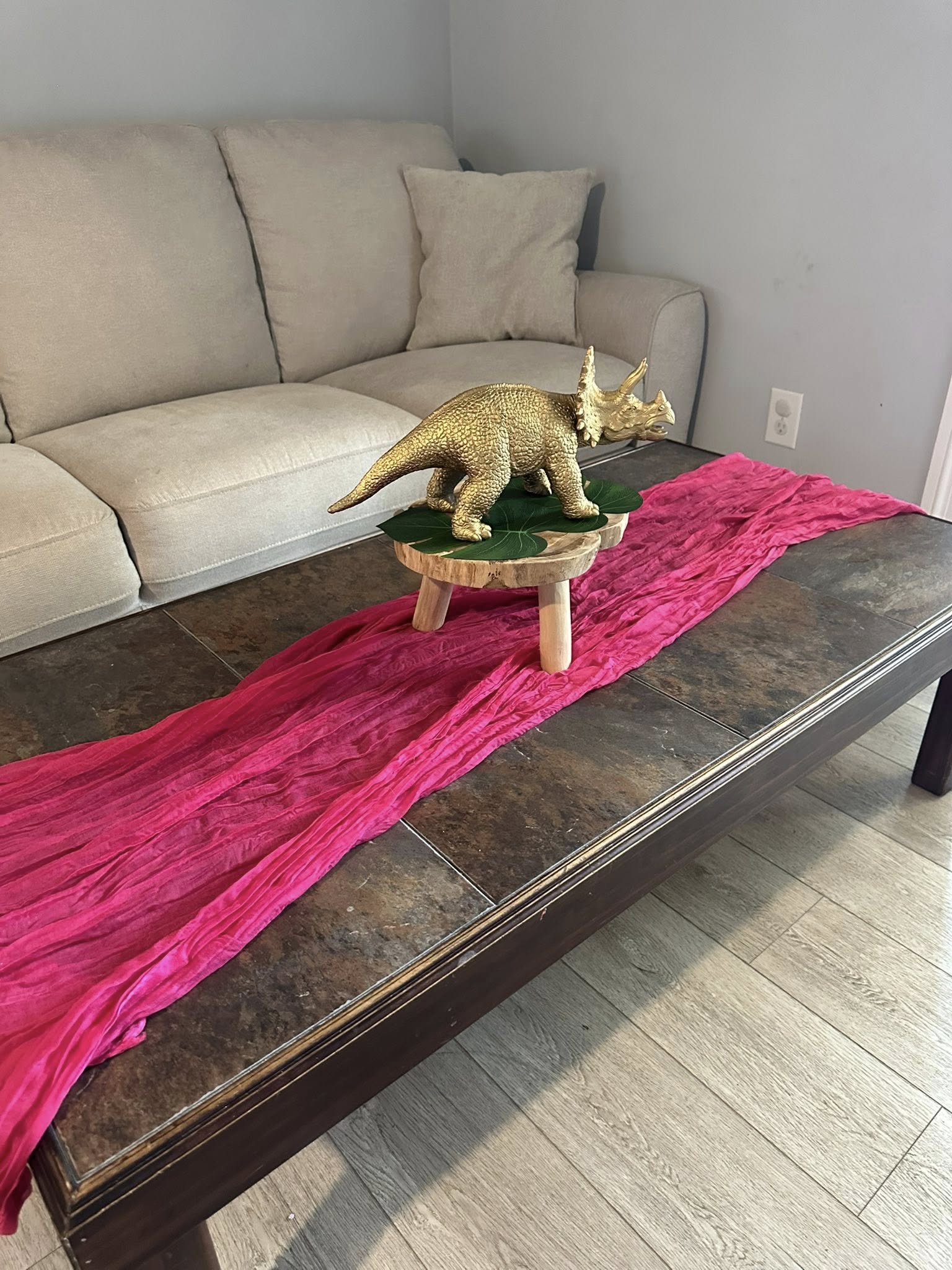 Gold triceratops dinosaur figurine on a wooden riser with a tropical leaf on a pink runner