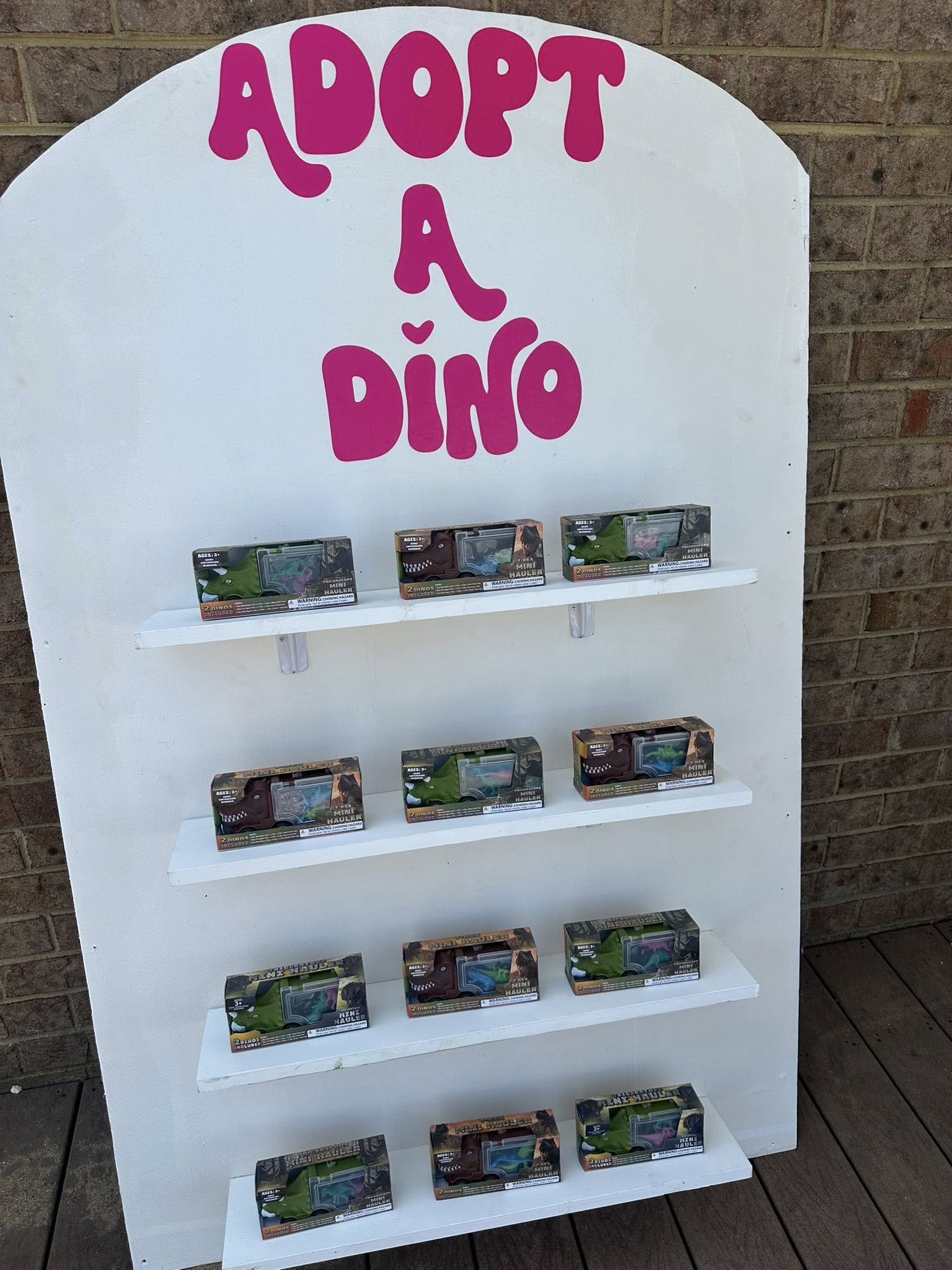 Adopt a Dino sign above shelves displaying boxed dinosaur toy hauler sets