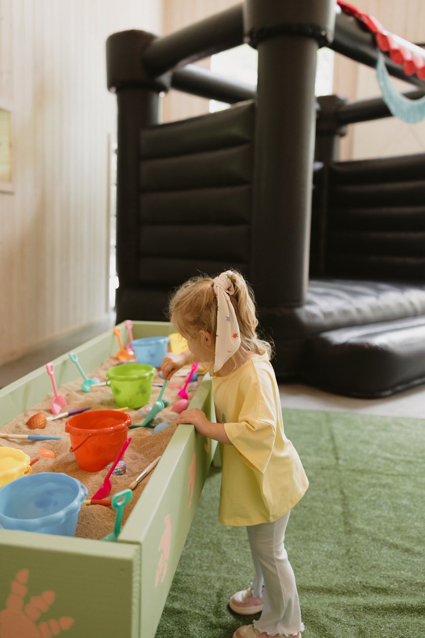 Young girl playing with colorful plastic shovels and buckets in an indoor sand table