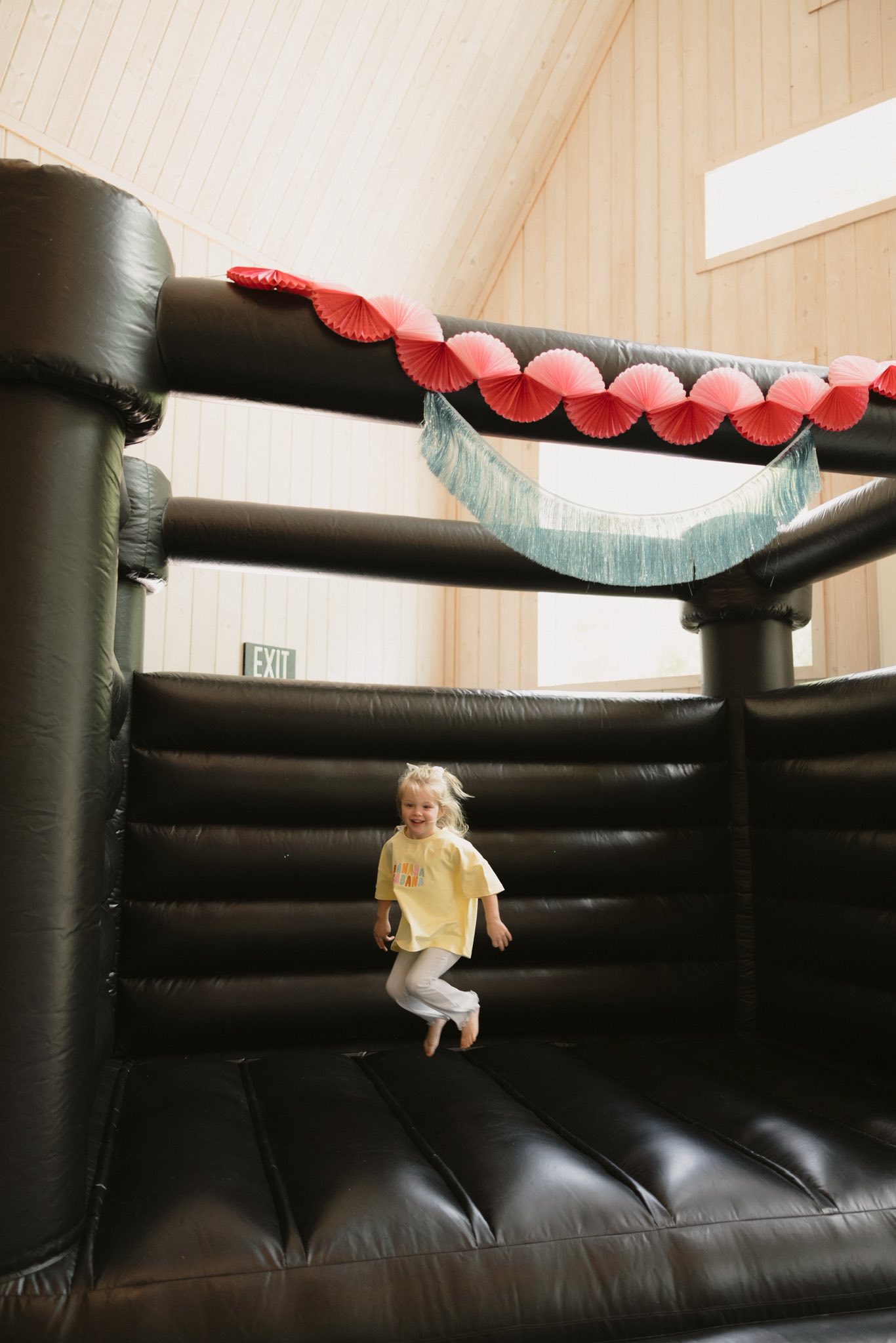 Young child in yellow shirt jumping inside a black bounce house decorated with pink and blue streamers