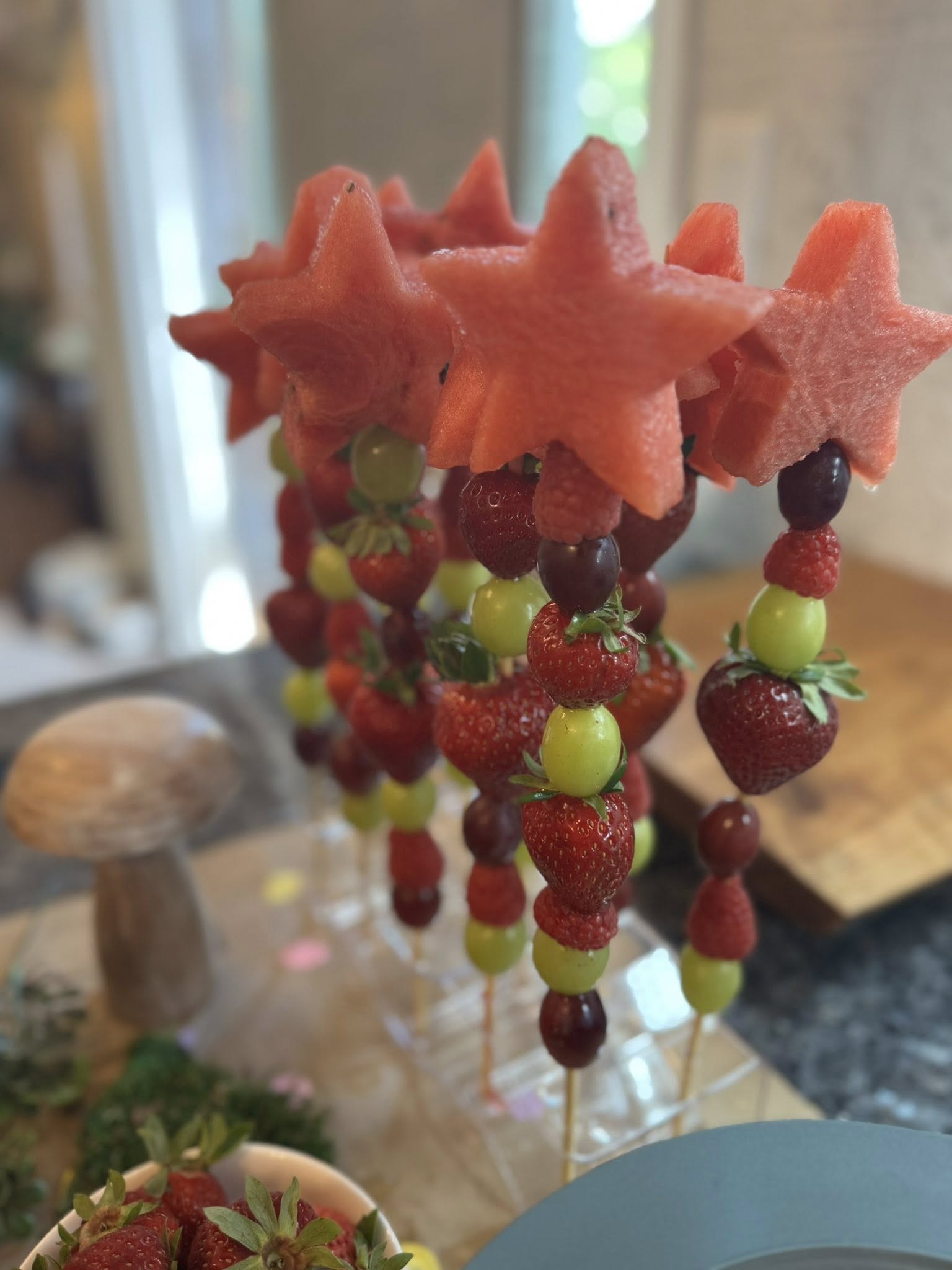 Fruit skewers with star-shaped watermelon pieces, fresh strawberries, and grapes.