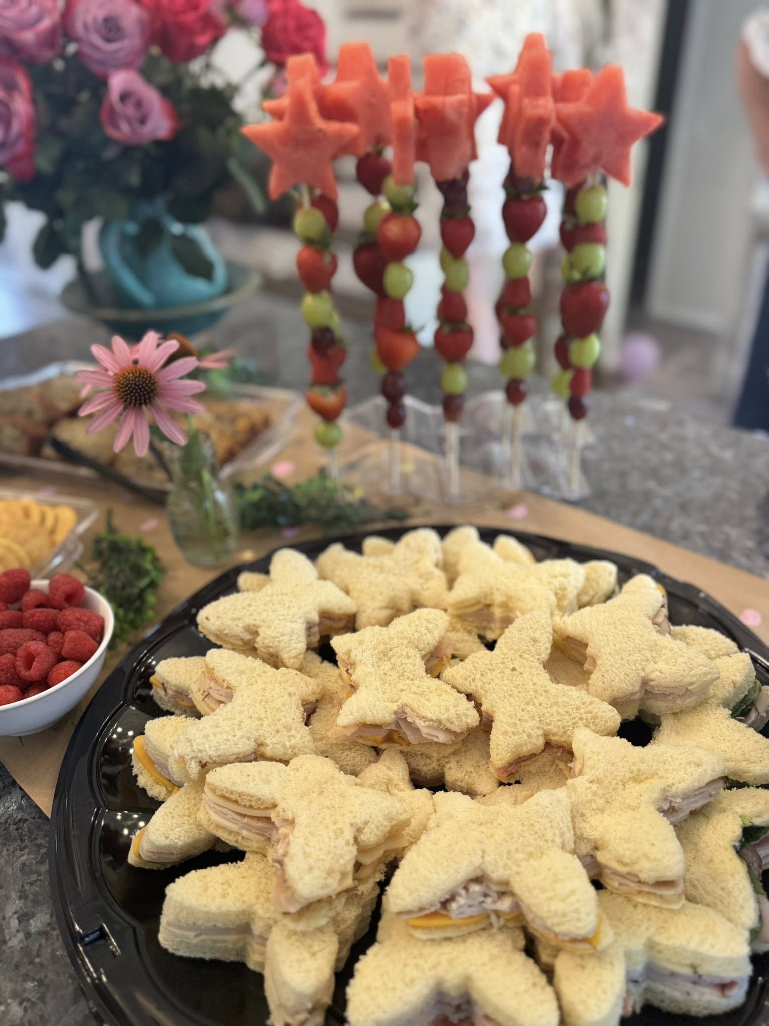 Platter of star-shaped turkey and cheese sandwiches with fruit skewers in the background for a party