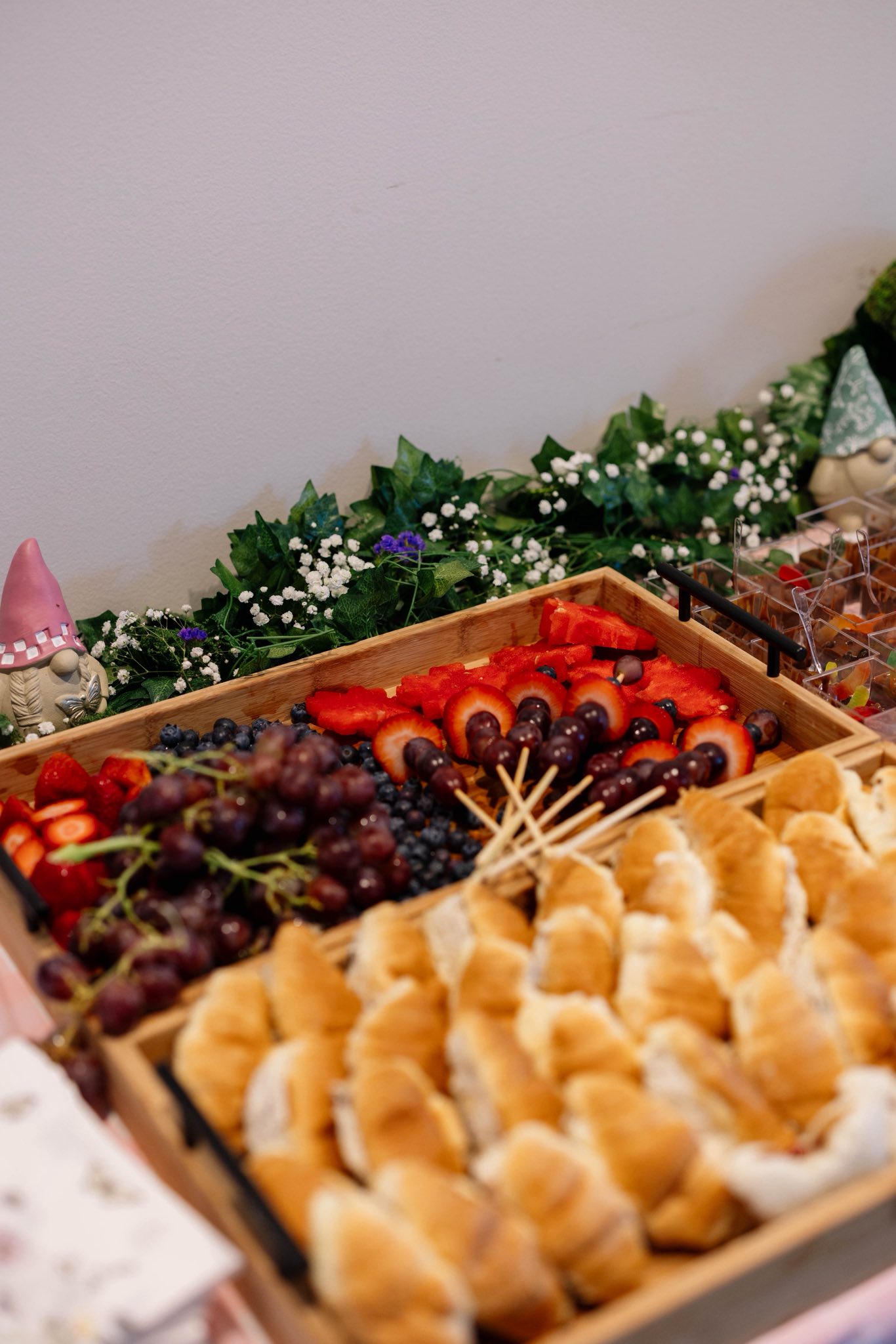 Catering trays featuring fresh grapes, strawberries, blueberries, and mini croissants arranged for a buffet.